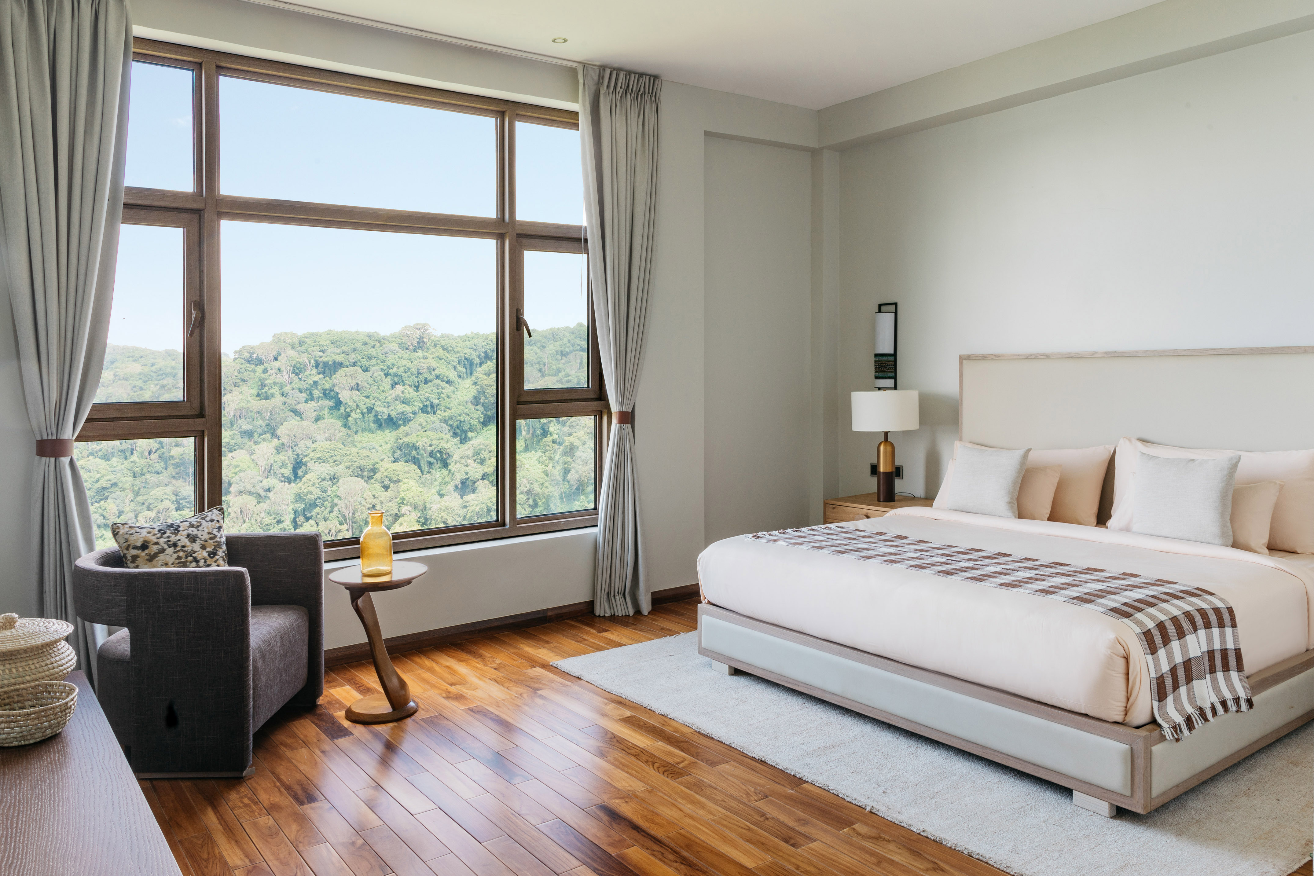 Modern hotel bedroom with forest view, king bed, and hardwood floor.