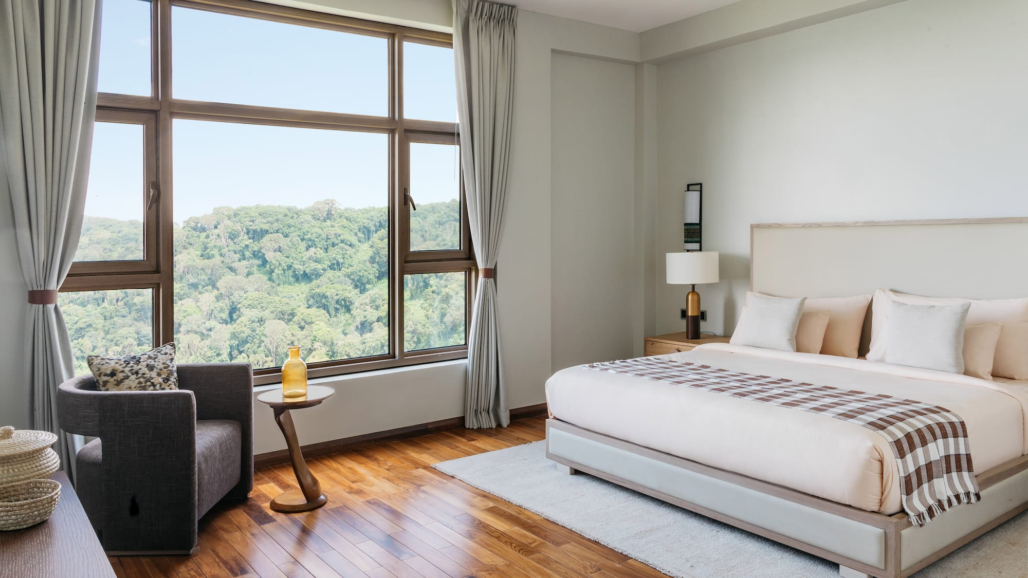 Modern hotel bedroom with forest view, king bed, and hardwood floor.