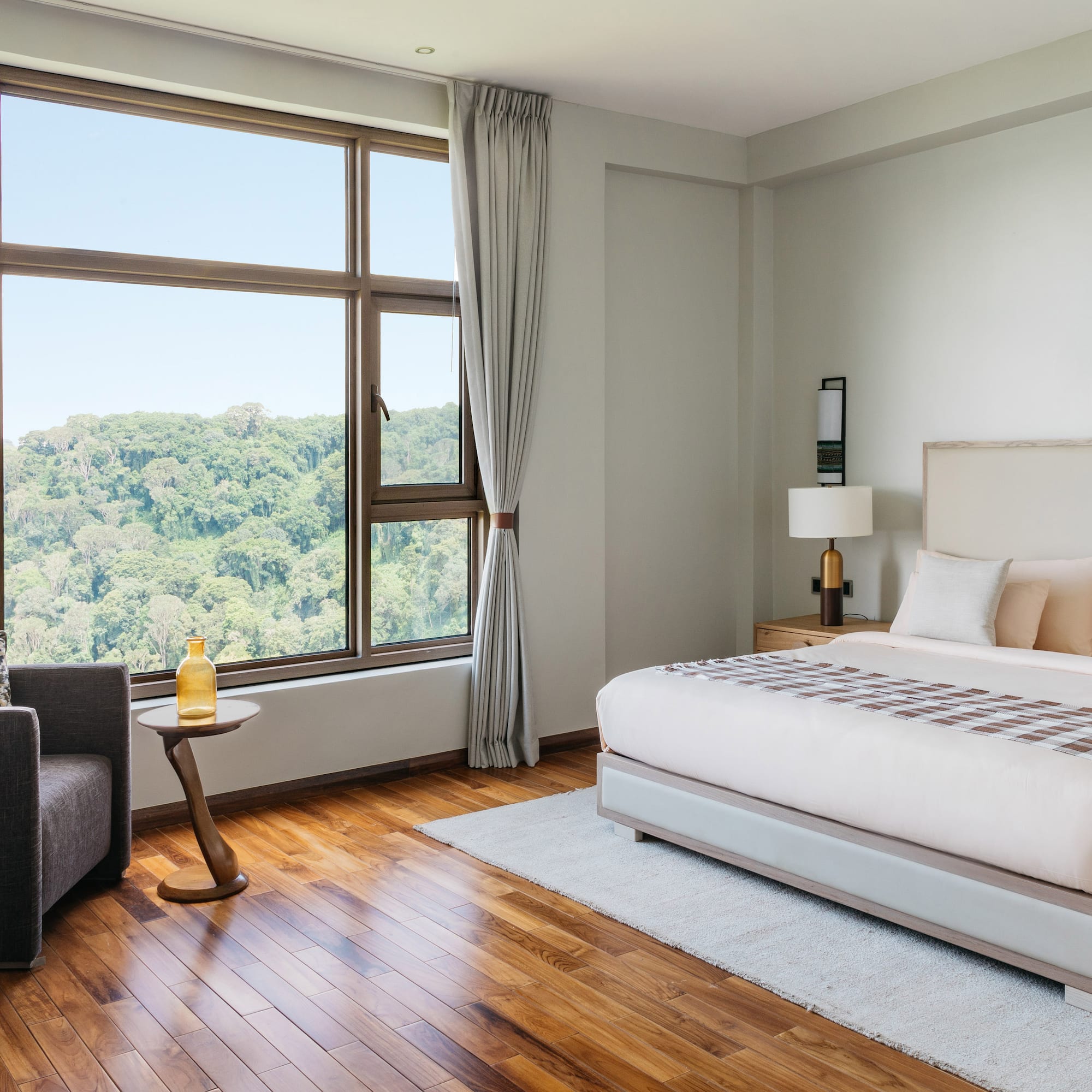 Modern hotel bedroom with forest view, king bed, and hardwood floor.