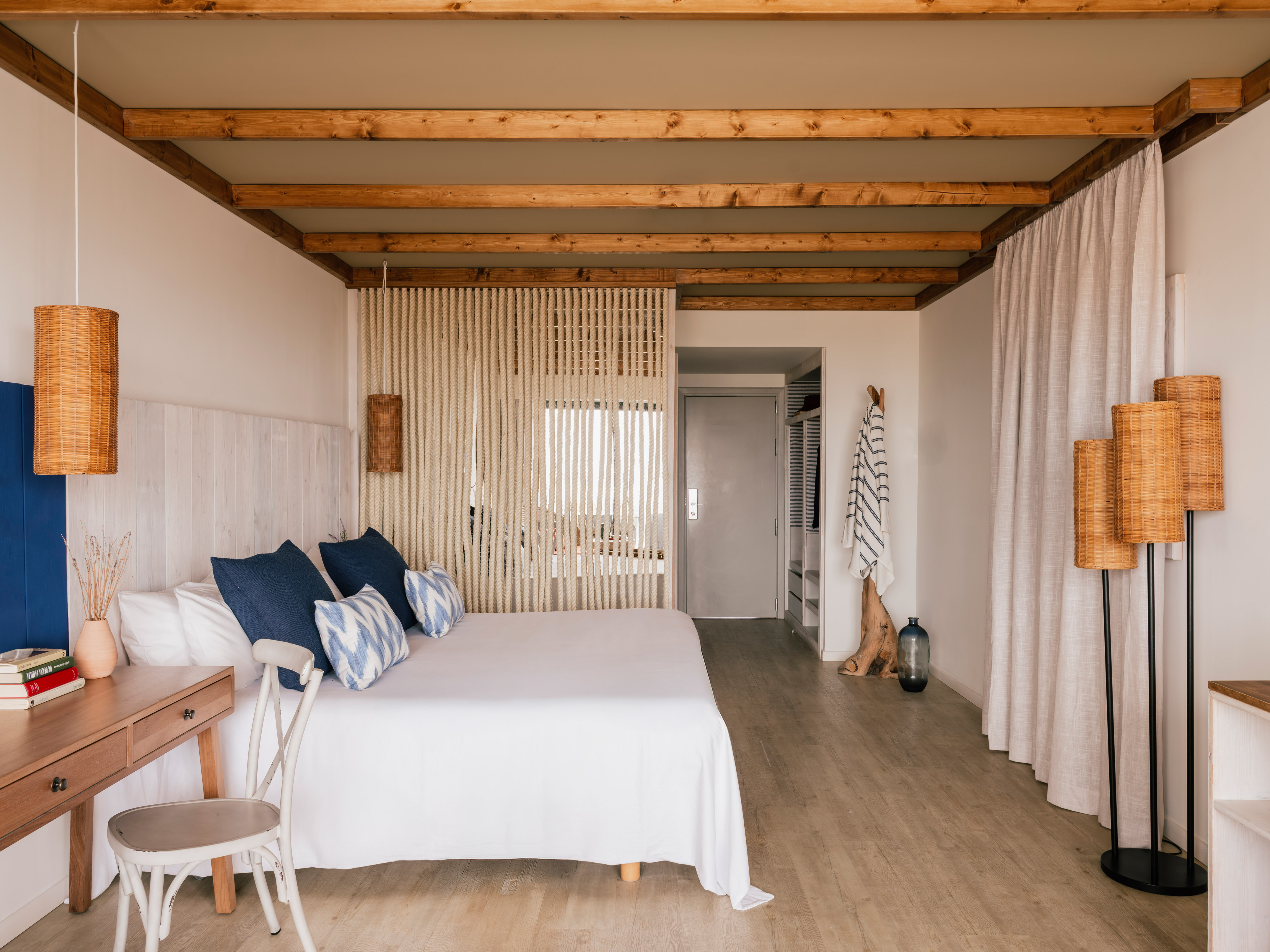 Habitación de hotel estilo costero: cama blanca, cojines azules, vigas madera.