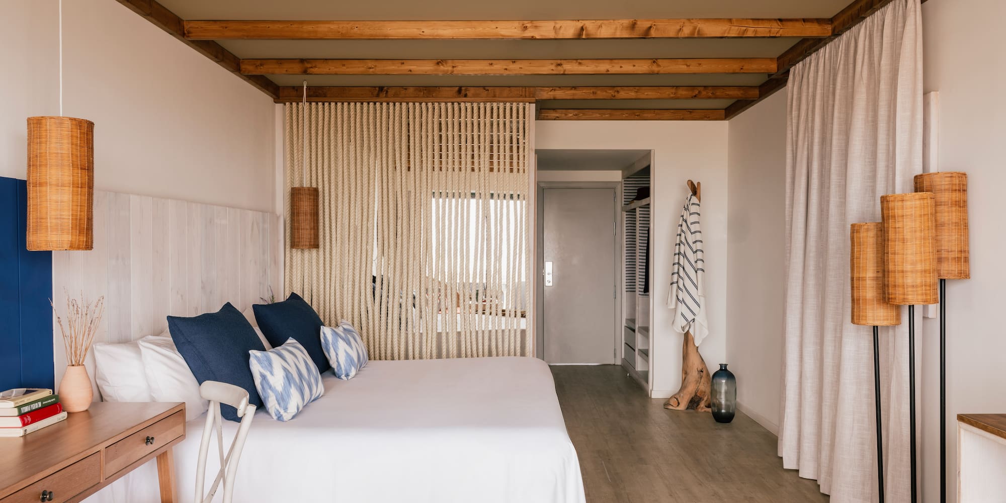 Habitación de hotel estilo costero: cama blanca, cojines azules, vigas madera.