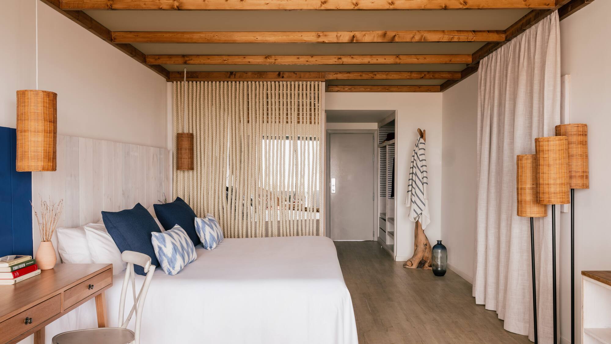 Habitación de hotel estilo costero: cama blanca, cojines azules, vigas madera.