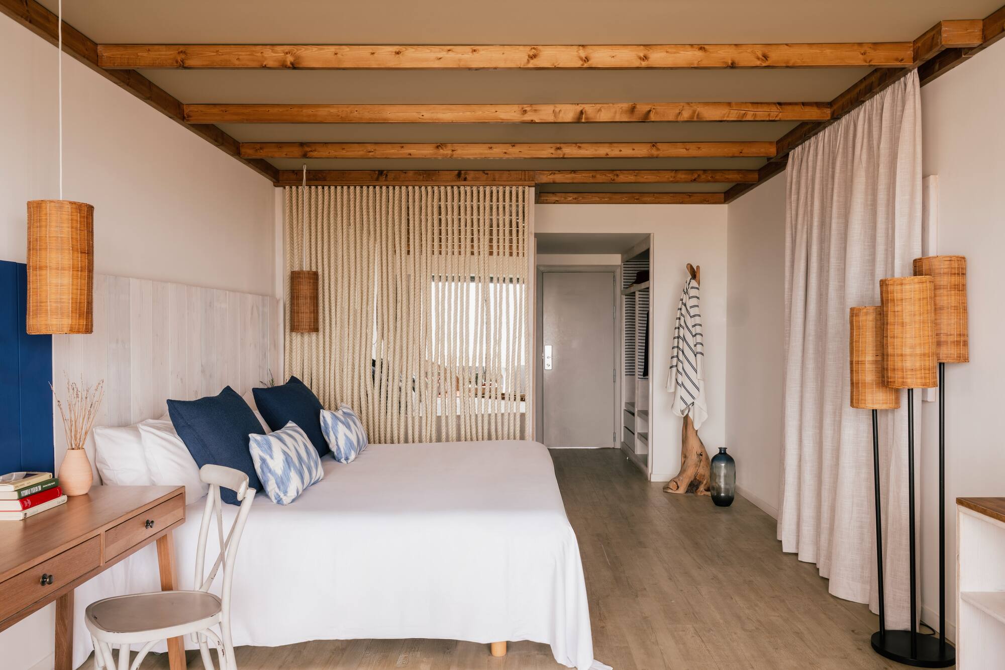 Habitación de hotel estilo costero: cama blanca, cojines azules, vigas madera.