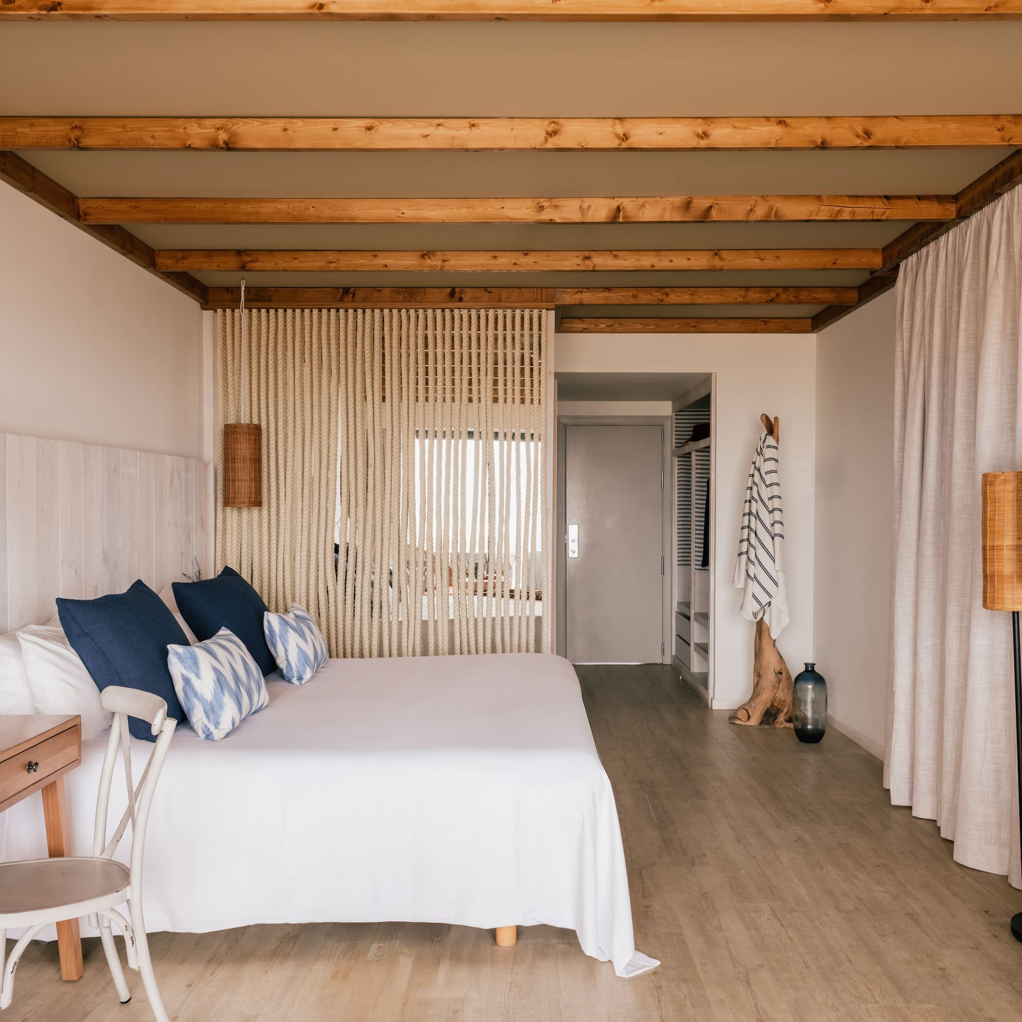 Habitación de hotel estilo costero: cama blanca, cojines azules, vigas madera.