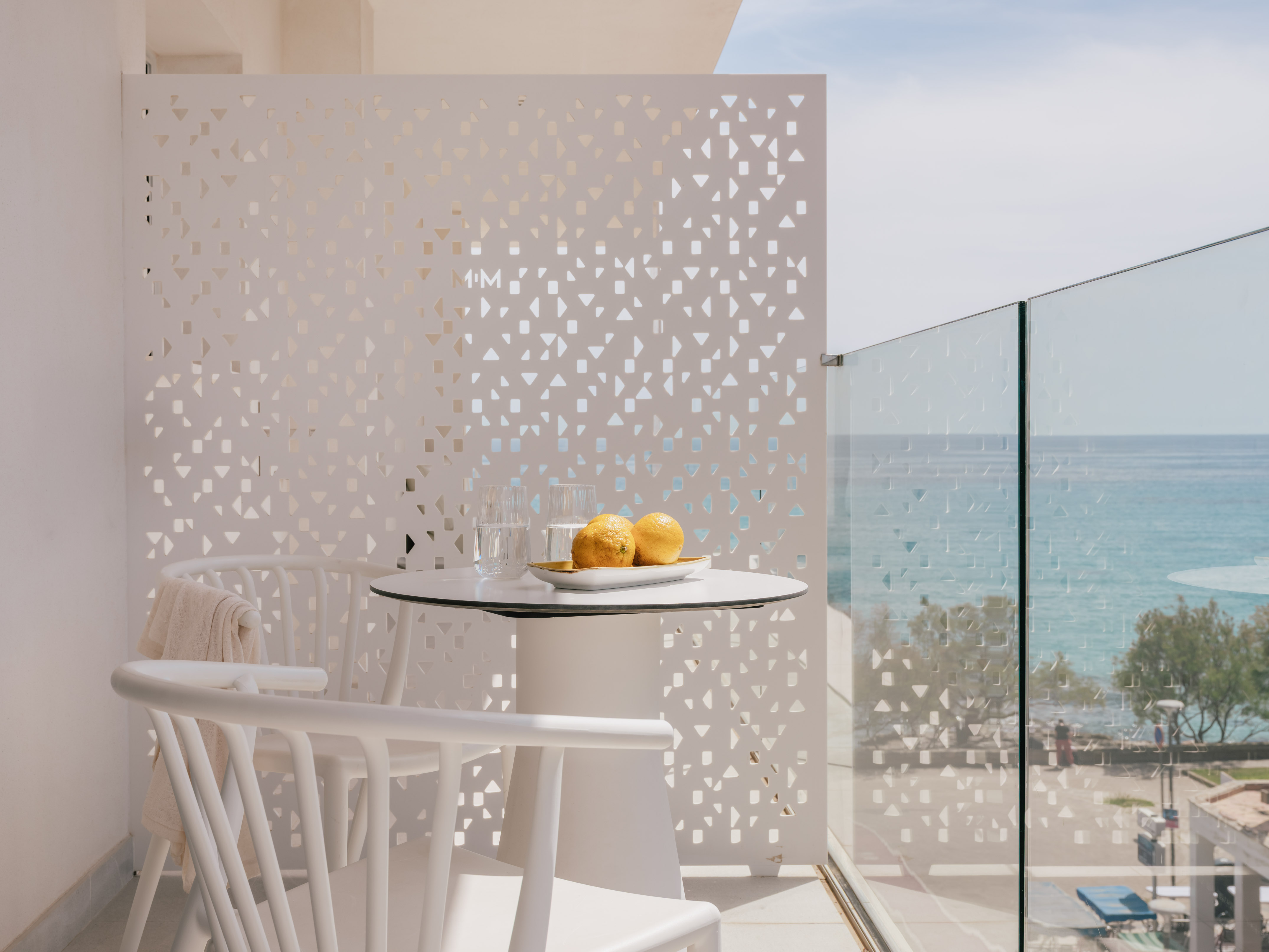 Balcón de hotel moderno con vista al mar, mesa blanca y limones.
