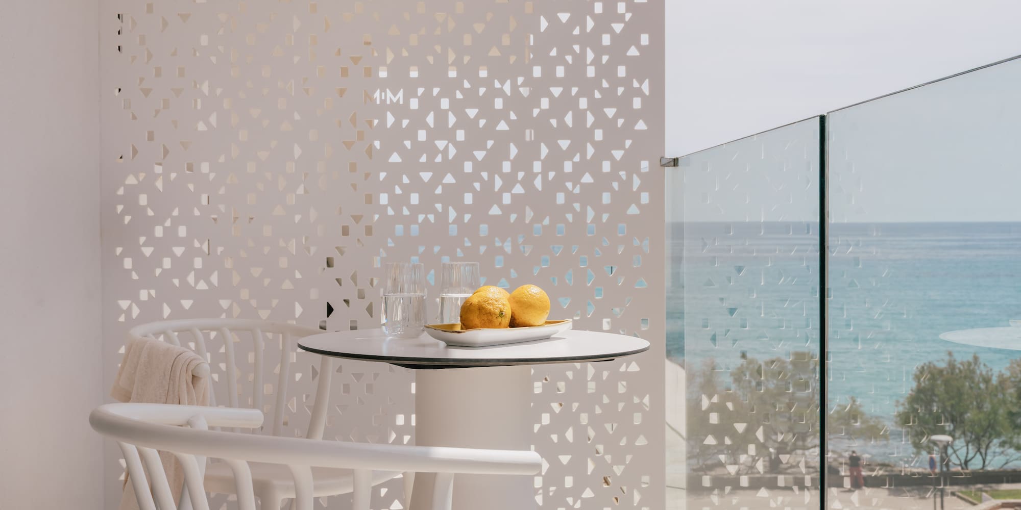 White modern balcony with sea view, table, chairs, and privacy screen.