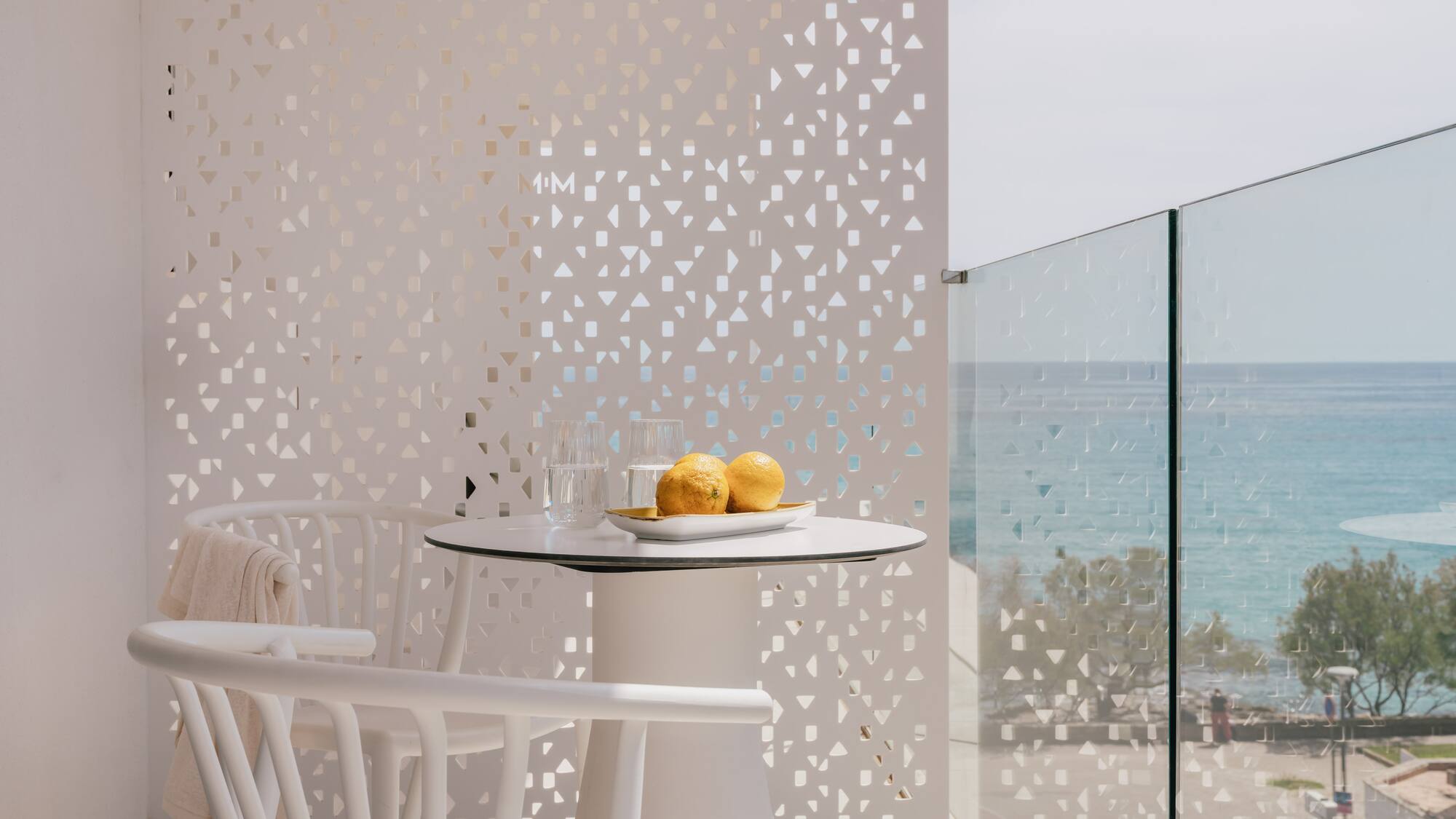 White modern balcony with sea view, table, chairs, and privacy screen.