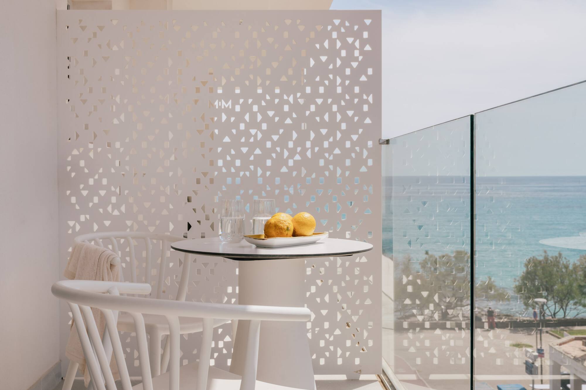 Balcón de hotel moderno con vista al mar, mesa blanca y limones.