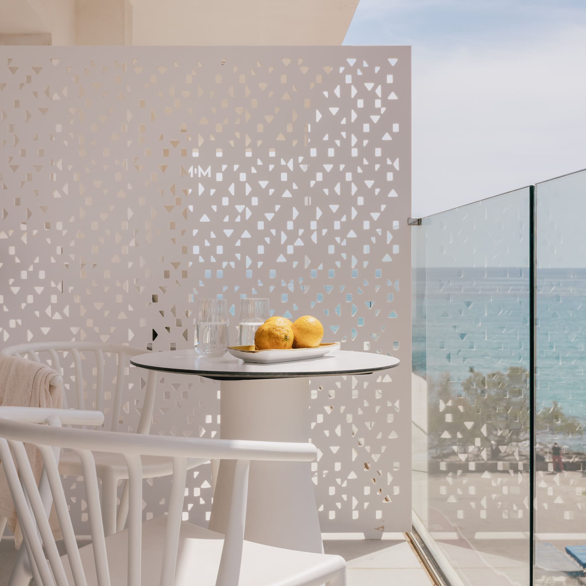 White modern balcony with sea view, table, chairs, and privacy screen.