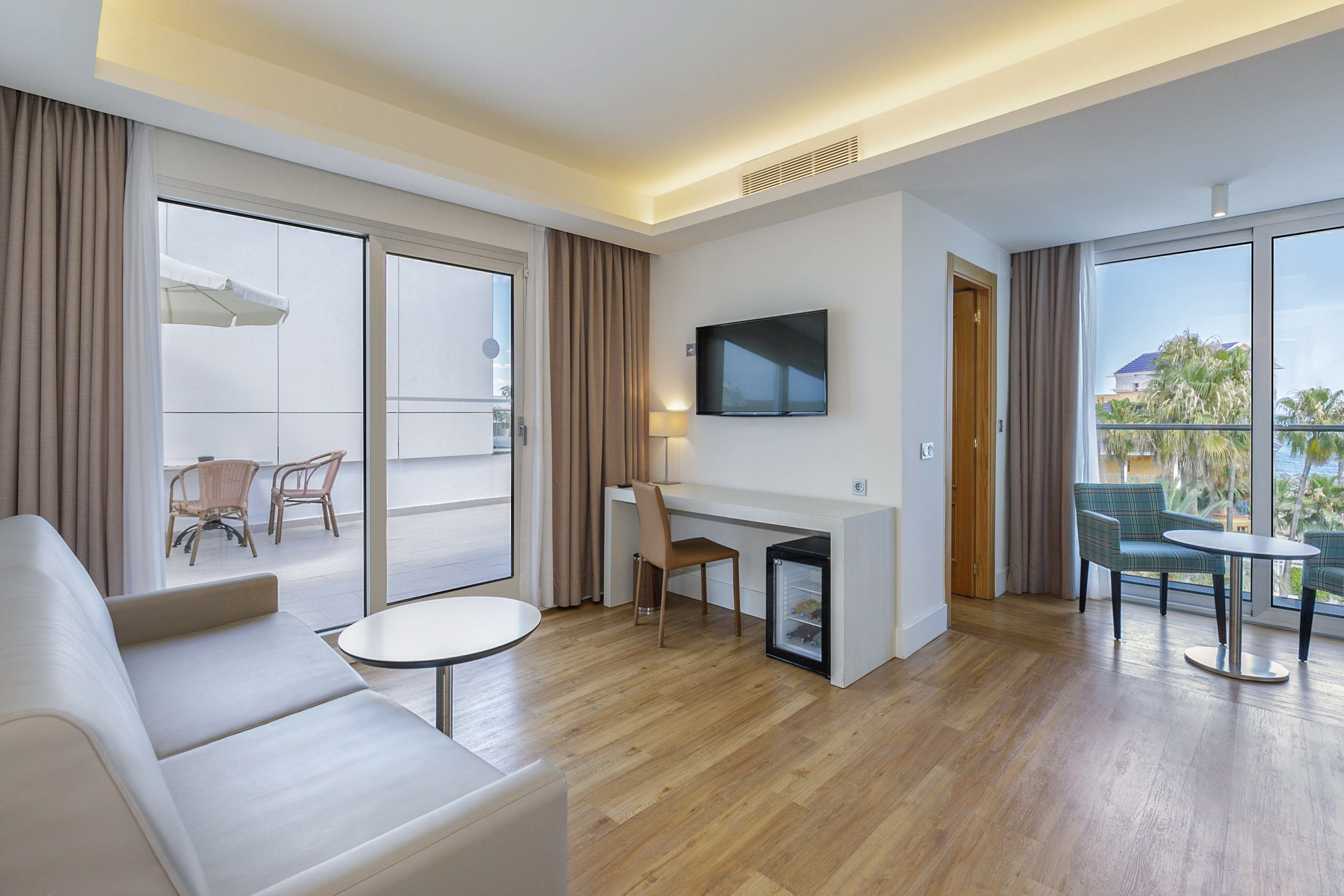 Modern hotel suite living room with sofa, desk, balcony, and sea view.