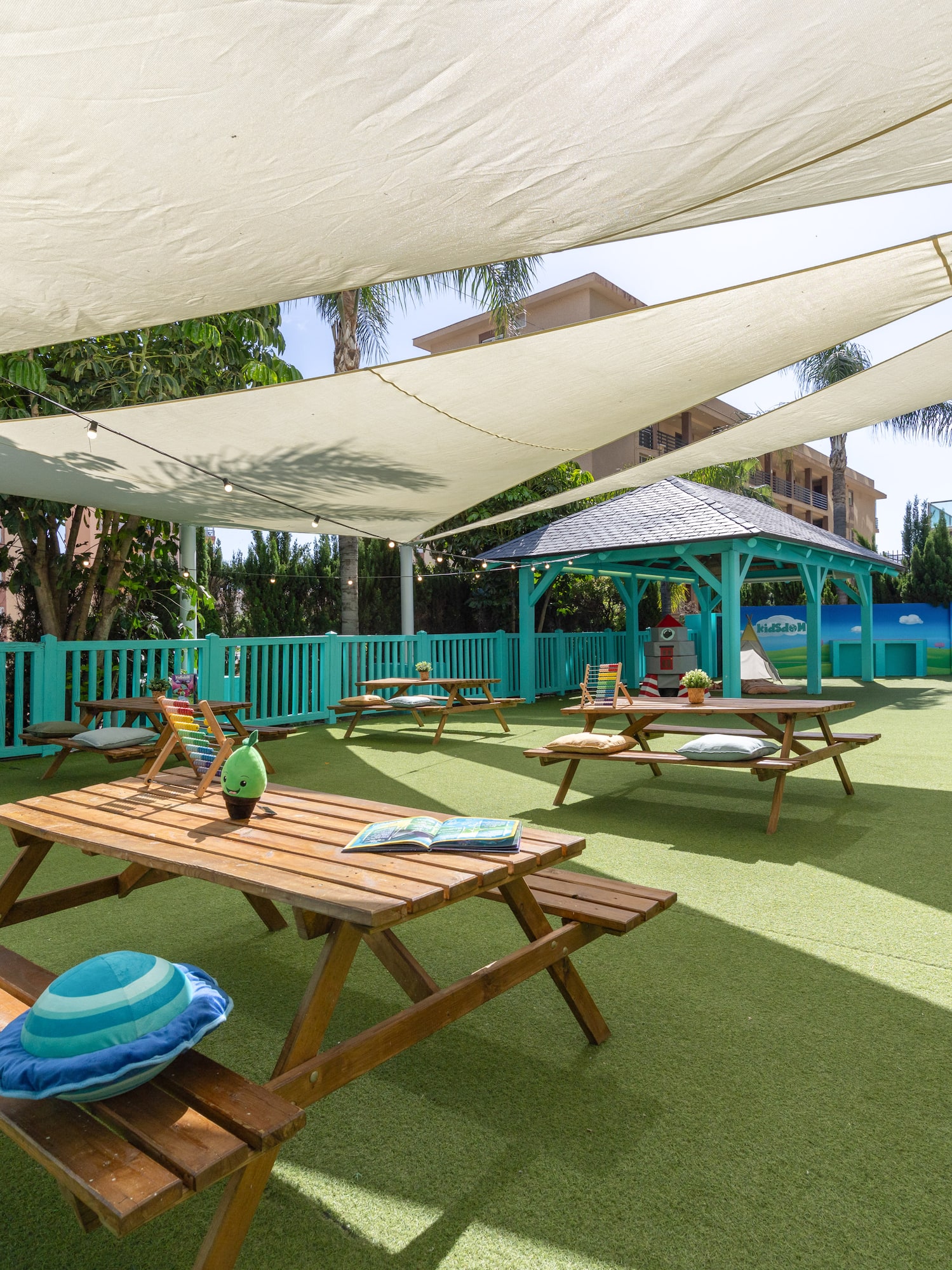 Outdoor kids play area with shade sails, picnic tables, and a 'Seeds Garden' mural.