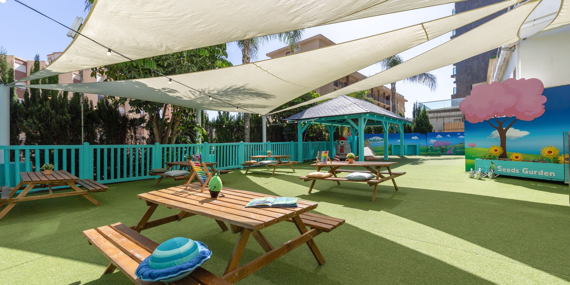 Kids play area with shaded picnic tables, artificial turf, and garden mural.