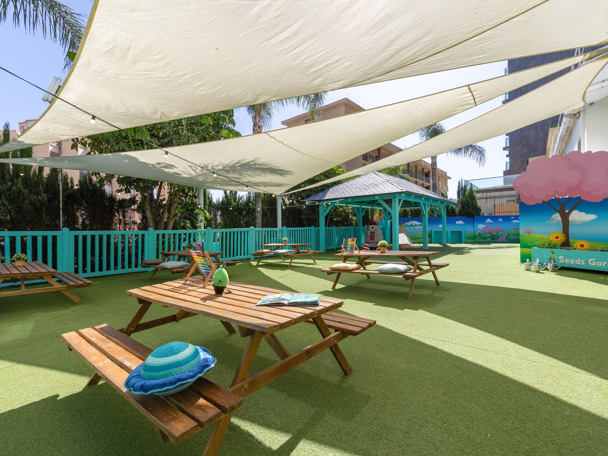 Kids' shaded outdoor playground with picnic tables and 'Seeds Garden' art.