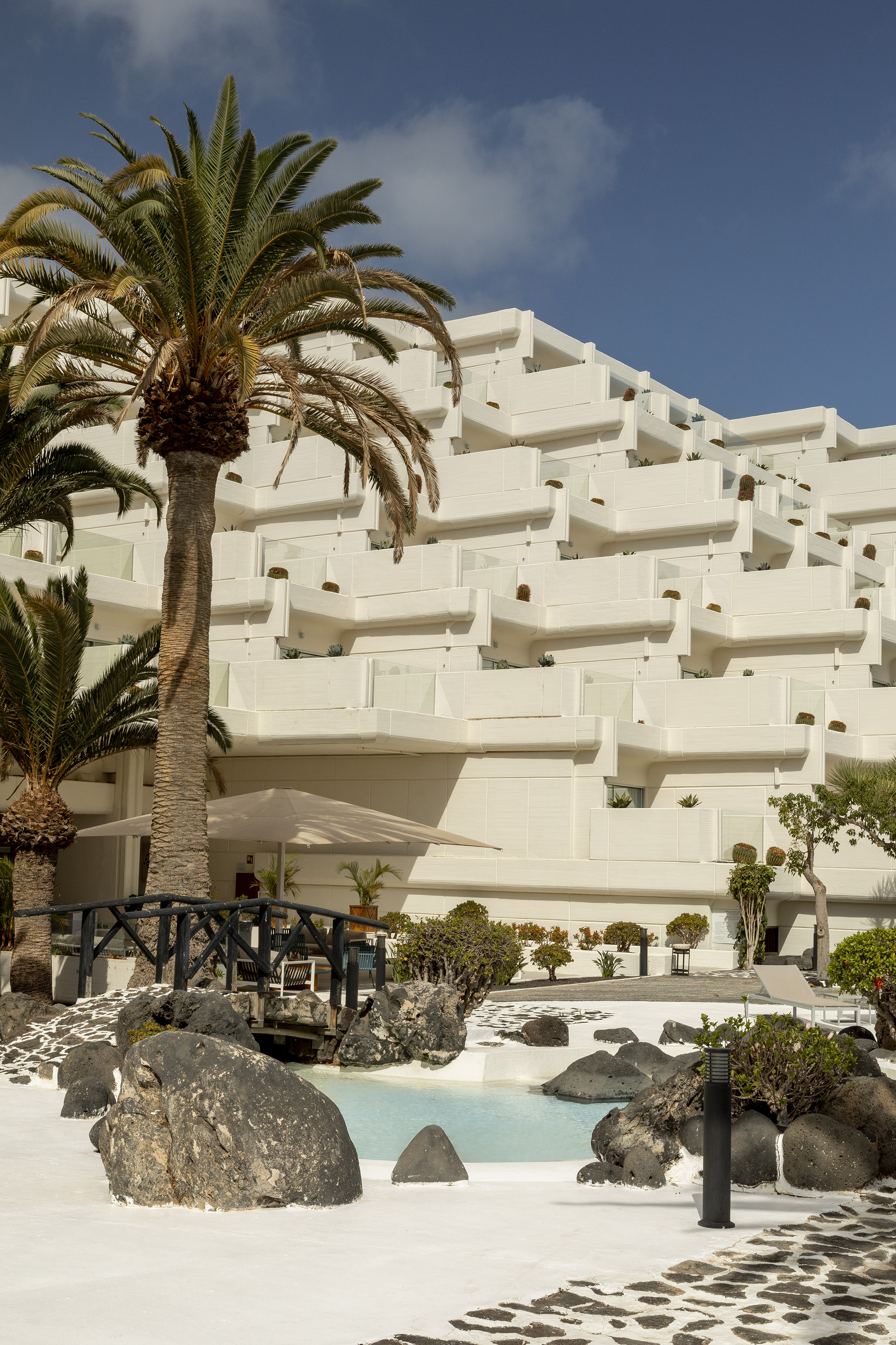 White tiered resort architecture, lush palm trees, serene pool with rocks.