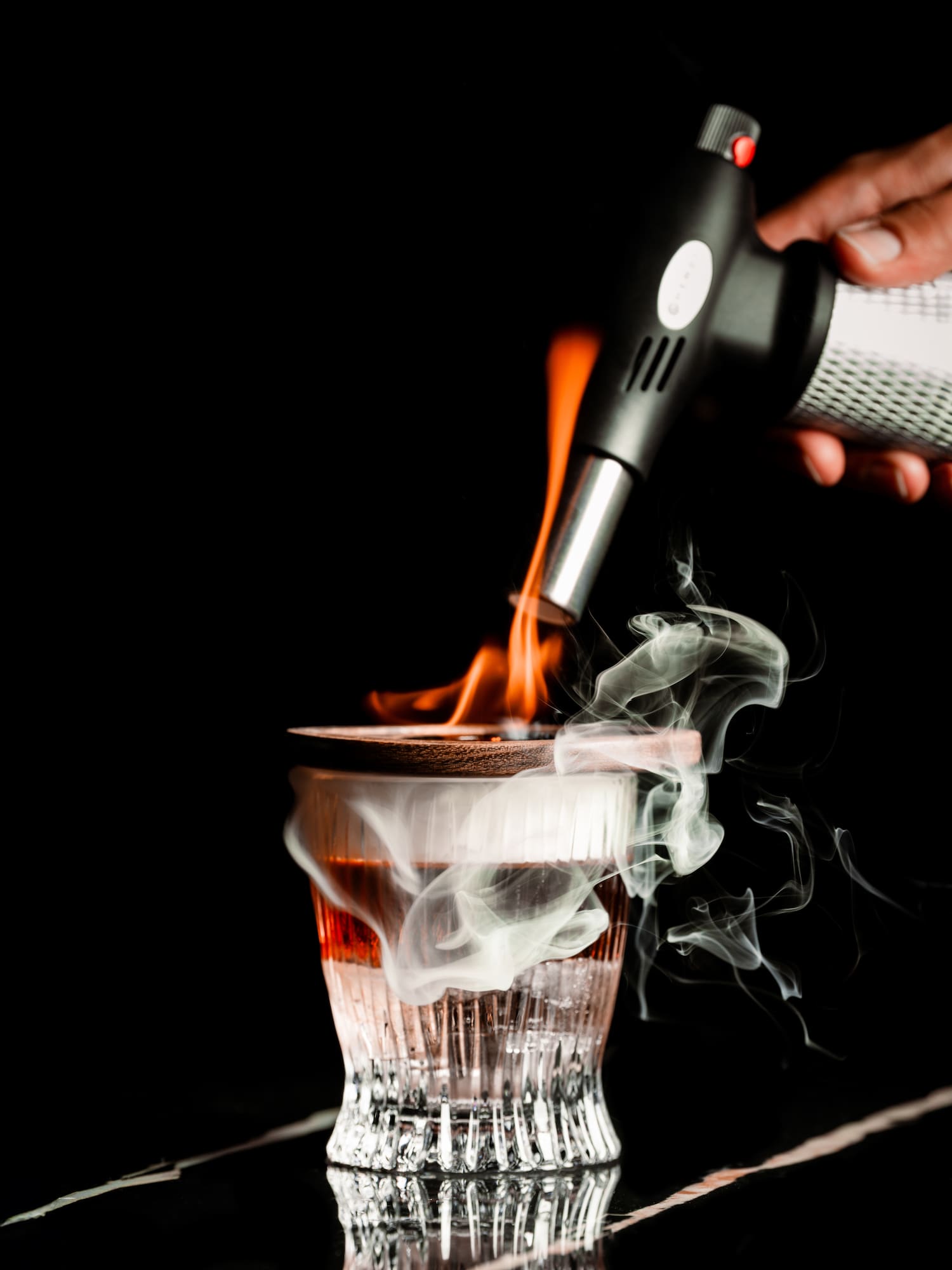 a hand holding a blowtorch over a glass with smoke