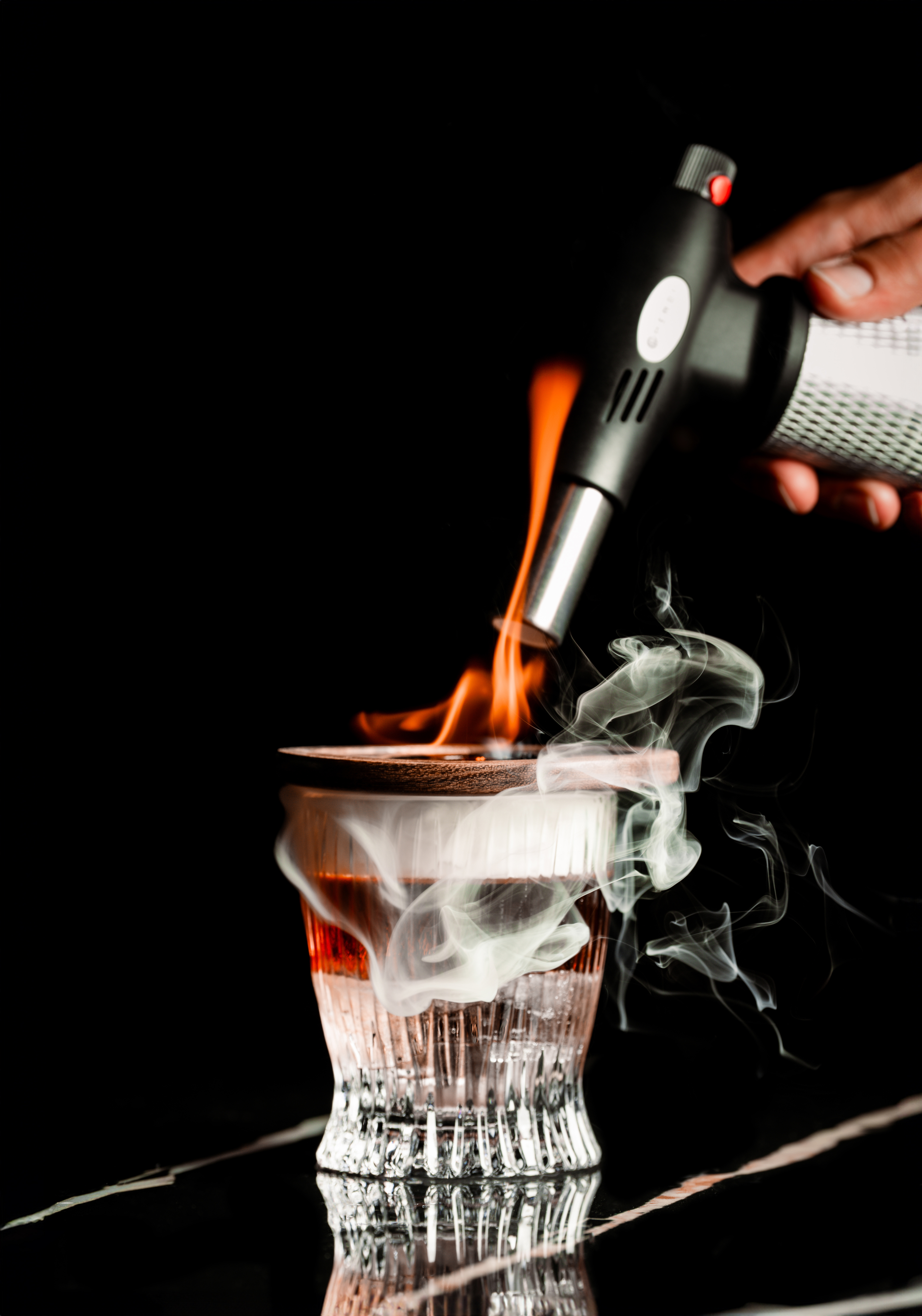 Hand smoking an Old Fashioned cocktail with a torch.