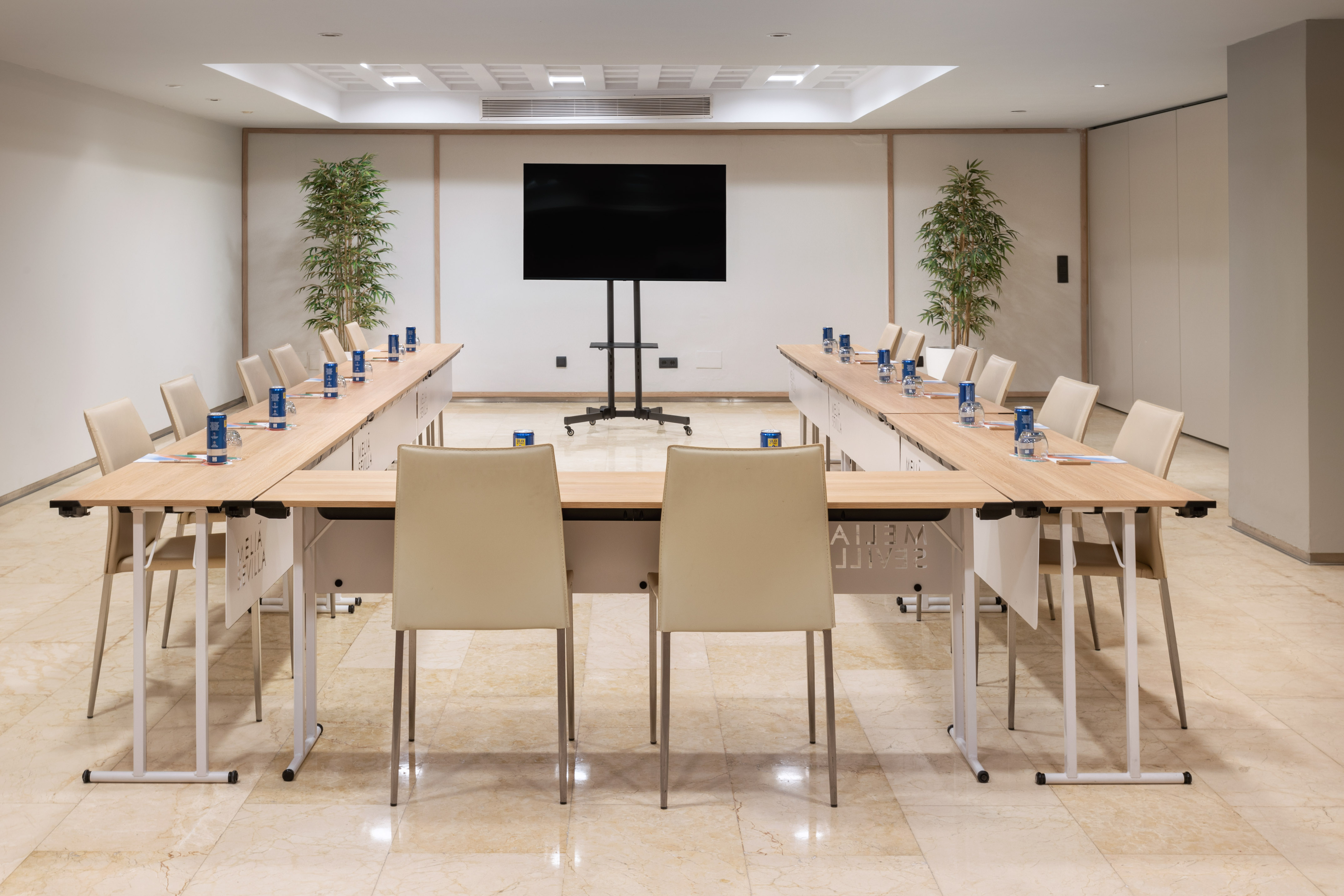 Modern meeting room with U-shaped tables, chairs, and presentation screen.