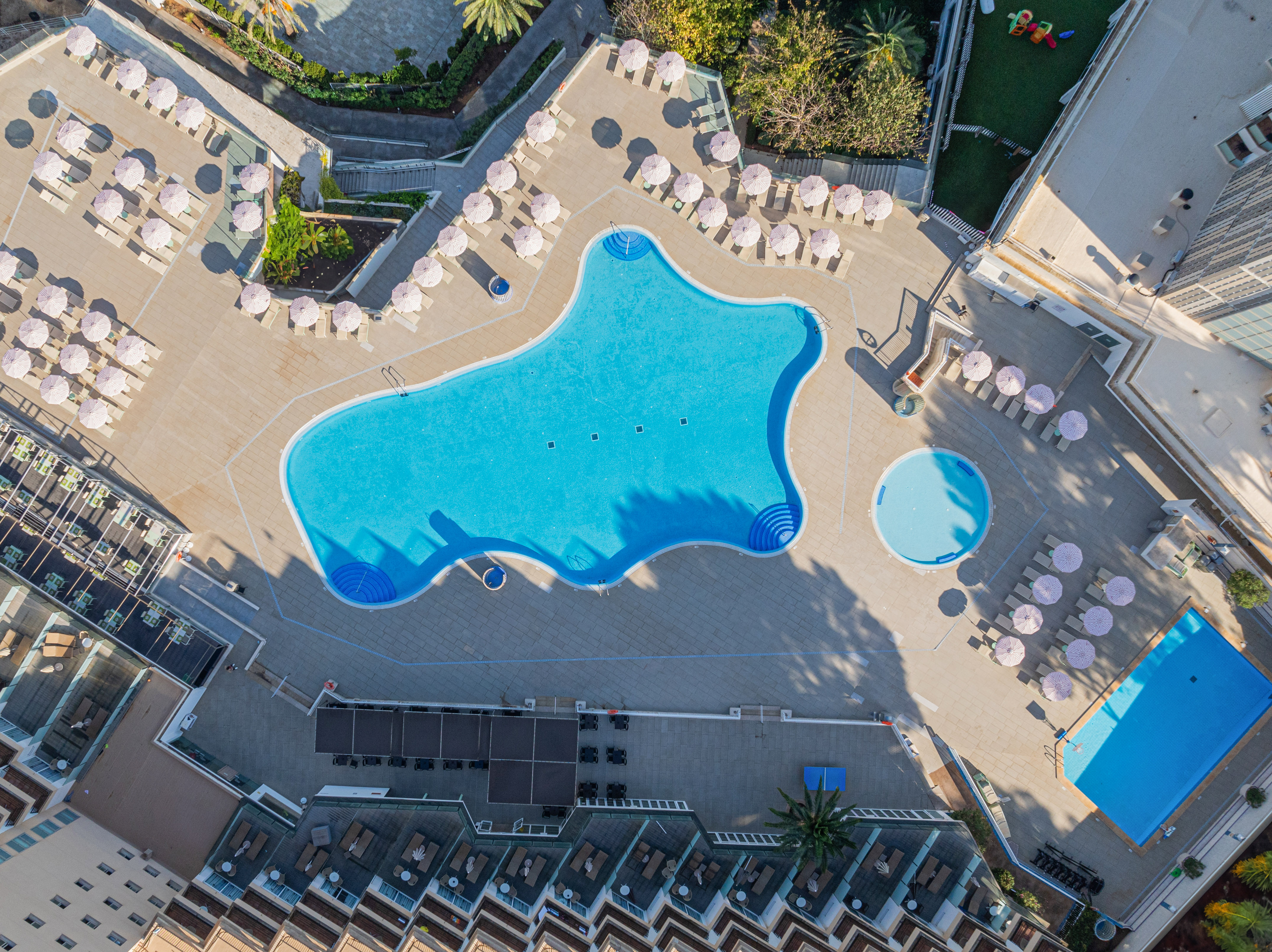 Aerial view of hotel resort pools with sun loungers and striped parasols.