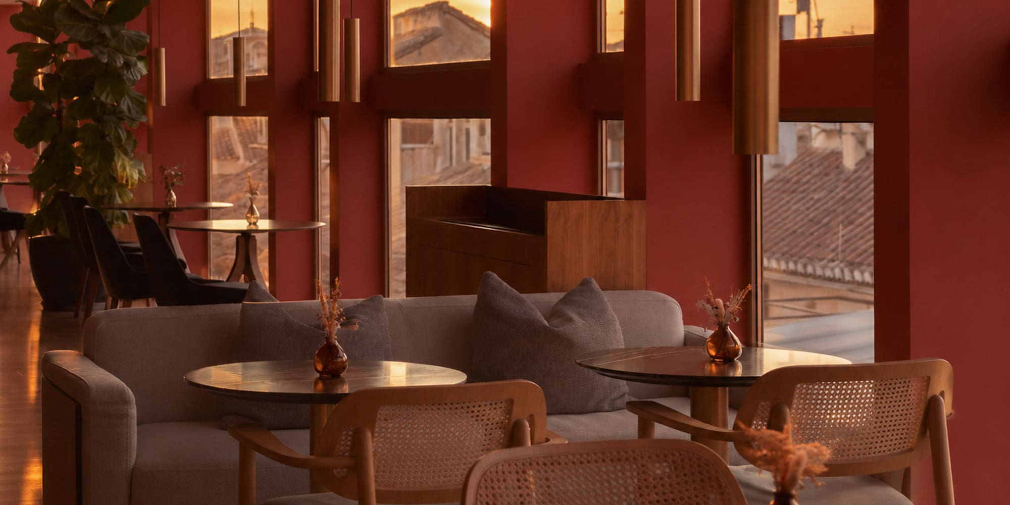 Red-walled lounge interior with sunset city view, modern seating, and pendant lights.
