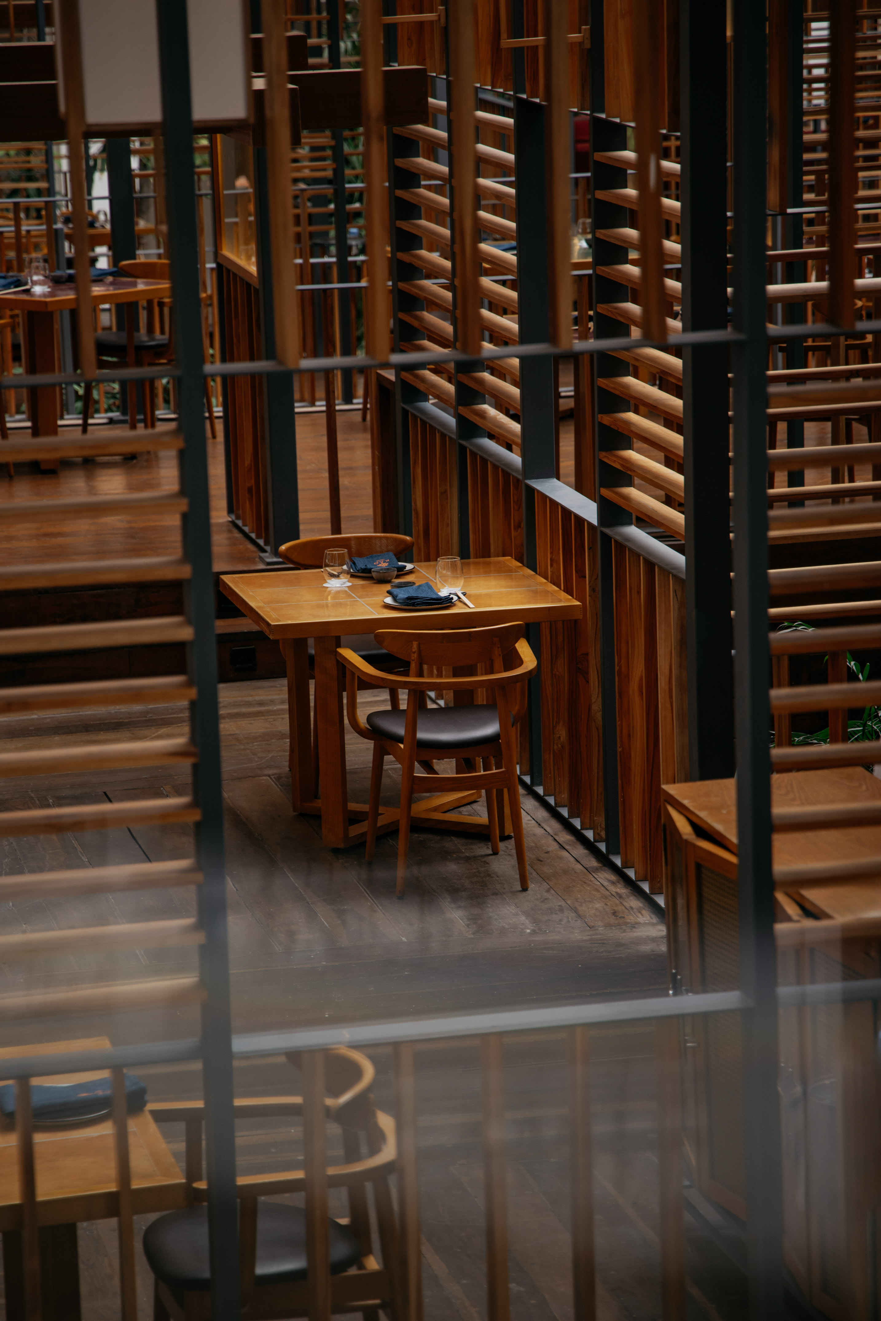 Wooden restaurant interior with dining tables, chairs, and slatted screens.