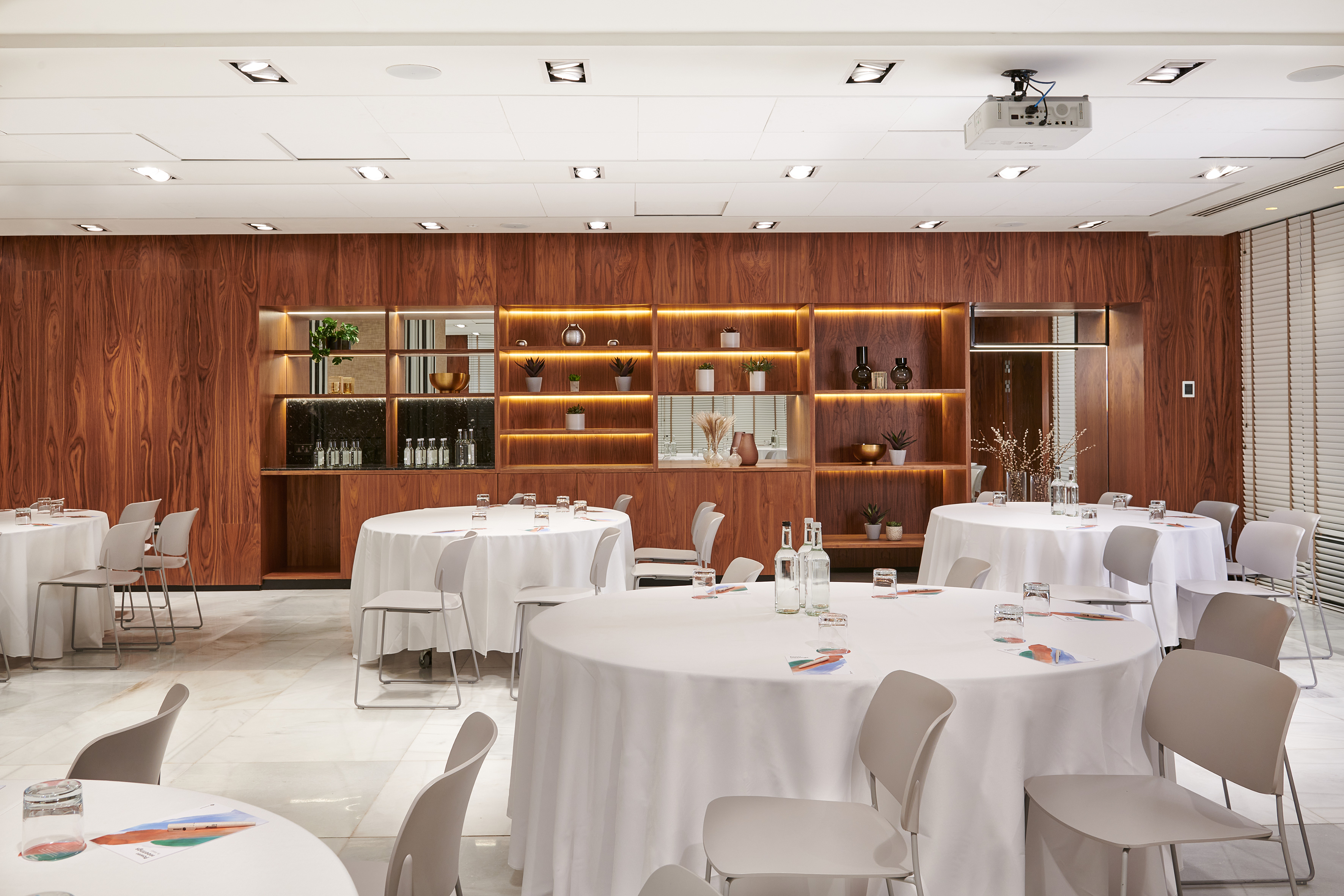 Modern conference room with round tables, grey chairs, wood-paneled walls, and projector.