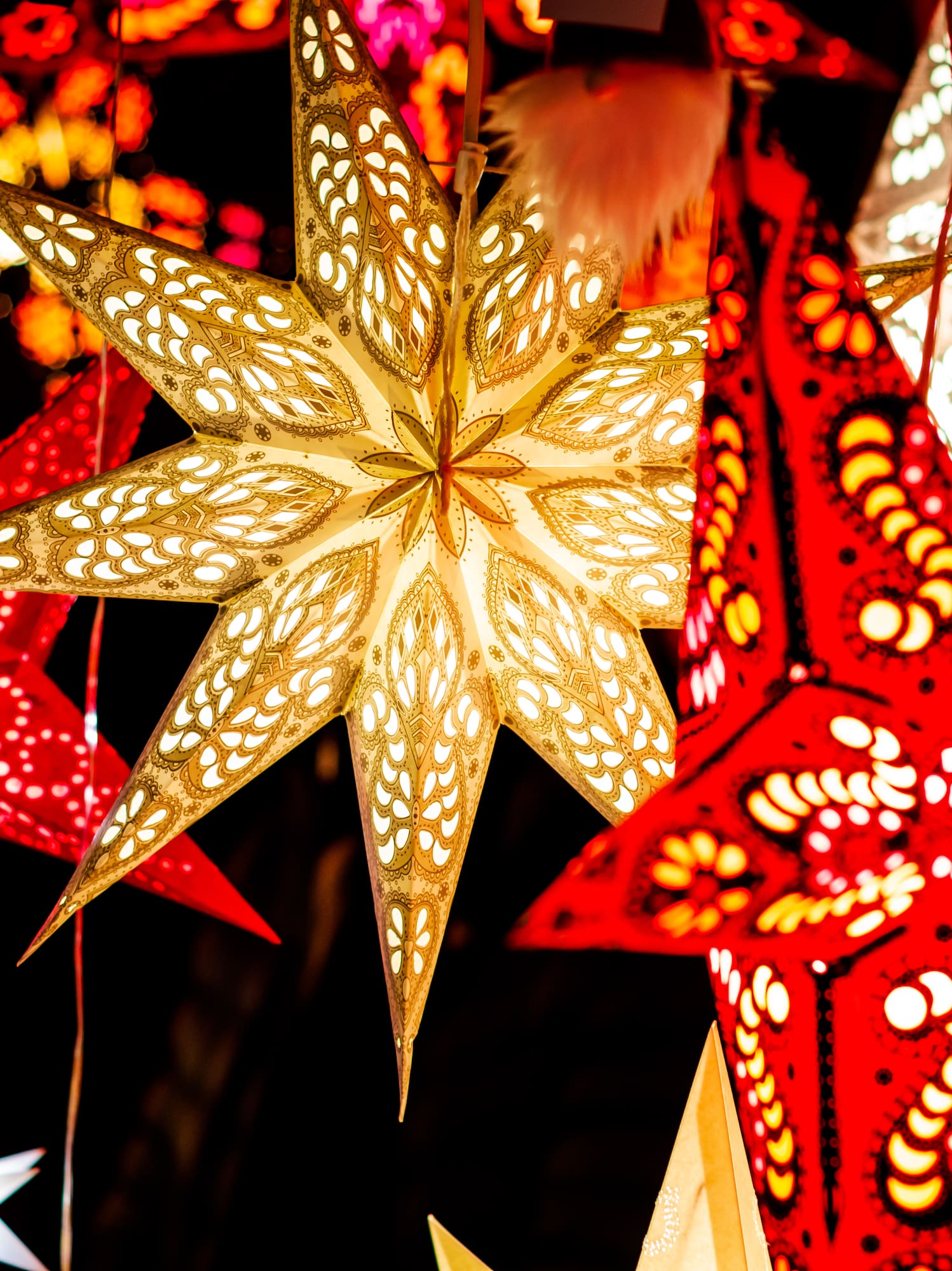 Festive glowing star lanterns in red, gold, and blue with intricate patterns.