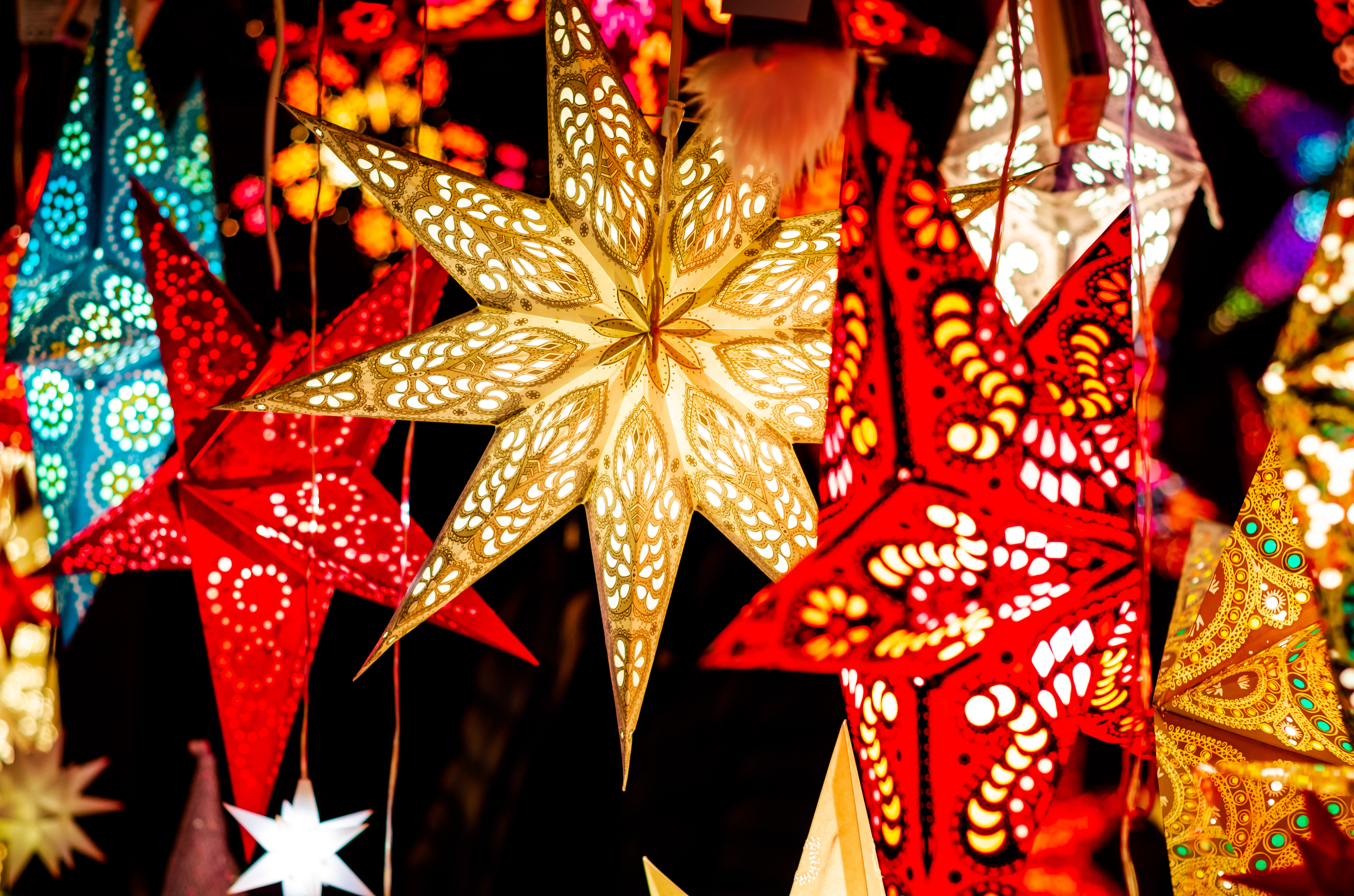 Festive glowing star lanterns in red, gold, and blue with intricate patterns.
