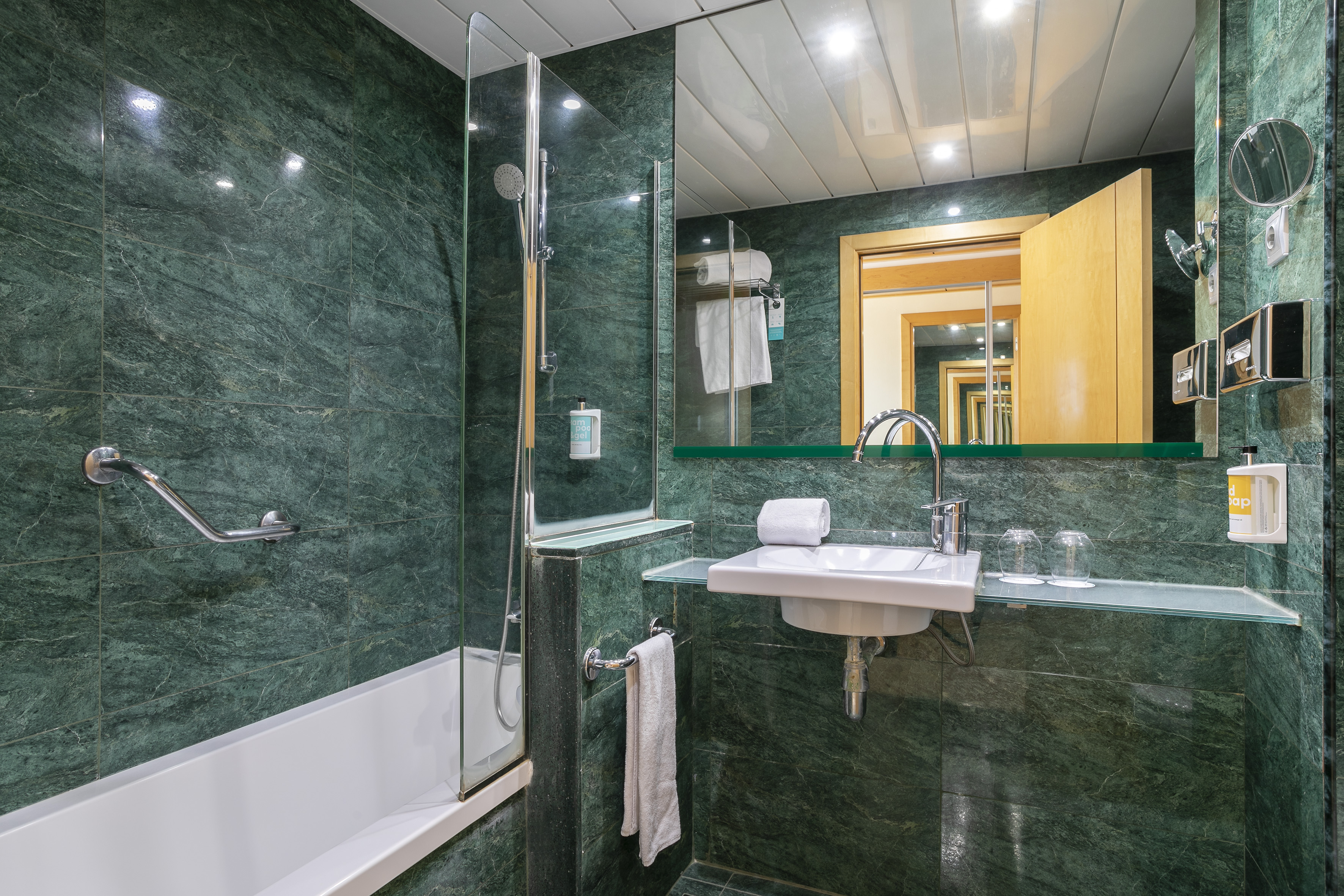 Green marble hotel bathroom with bathtub, shower, sink, and large mirror.