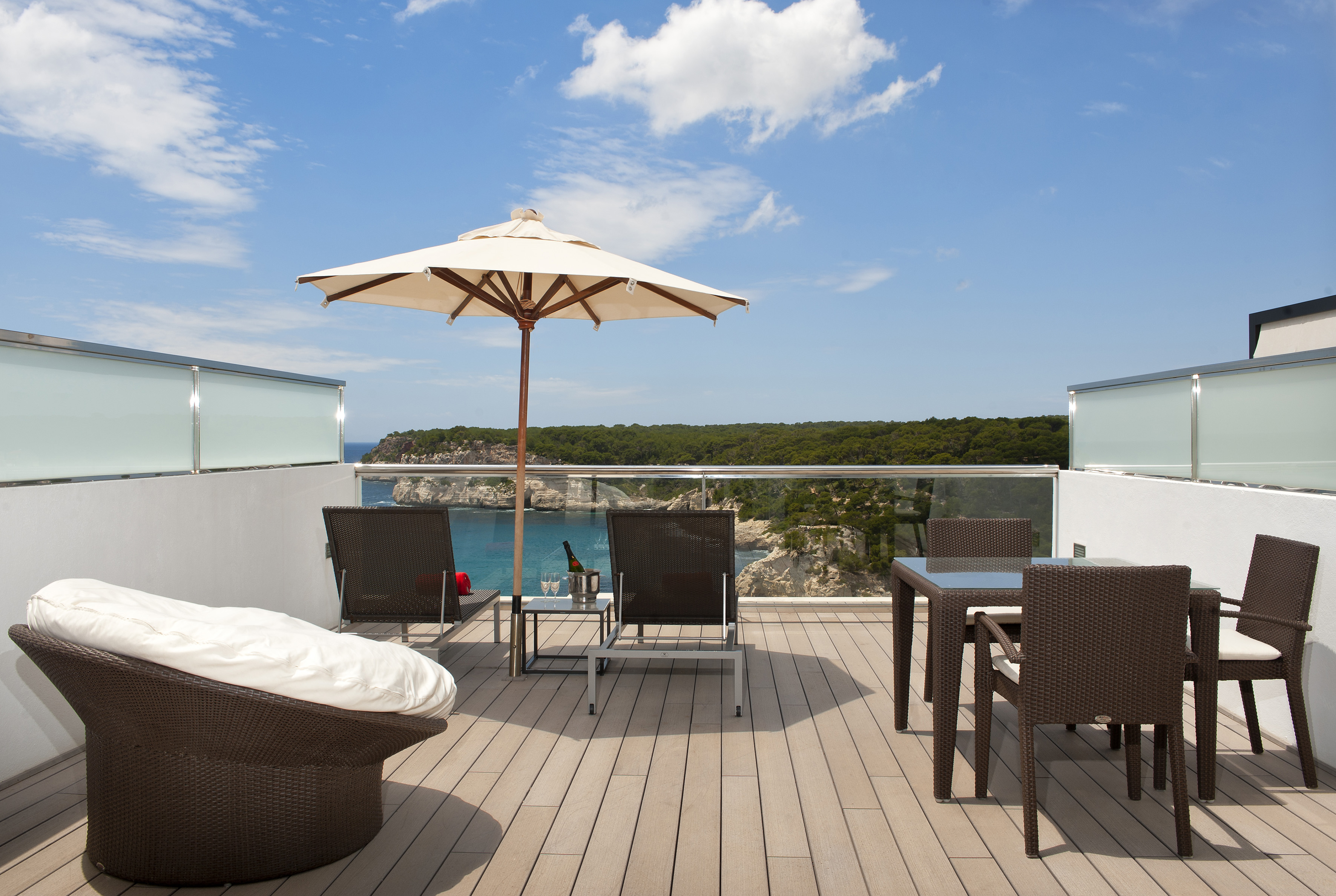 Balcony with ocean view, outdoor furniture, patio umbrella, overlooking cliffs.