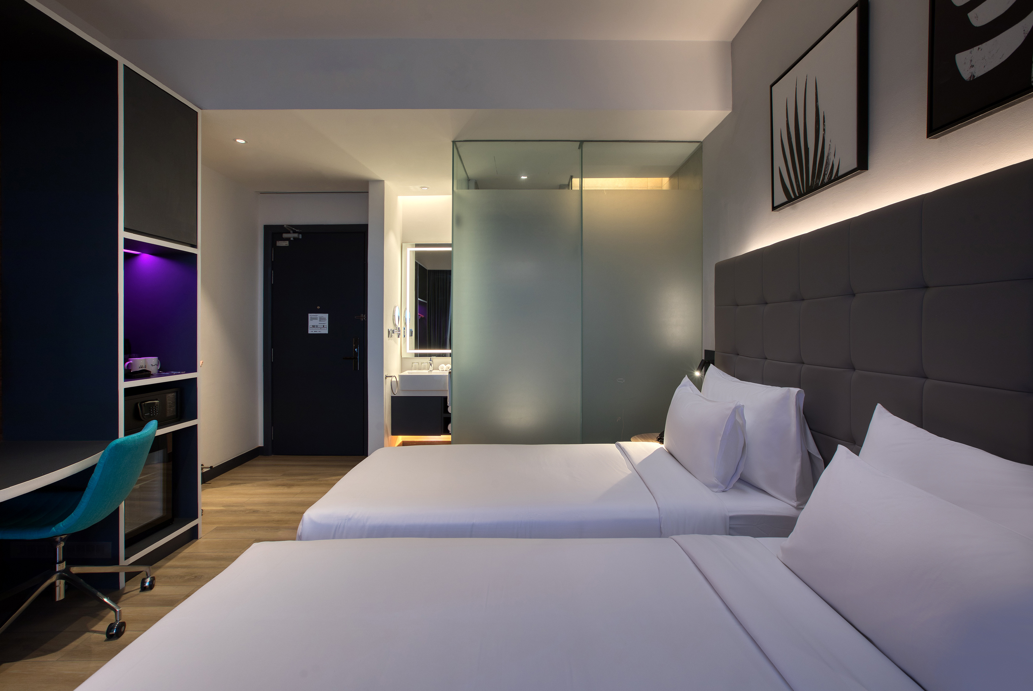 Modern hotel room with two twin beds, work desk, and frosted glass bathroom.