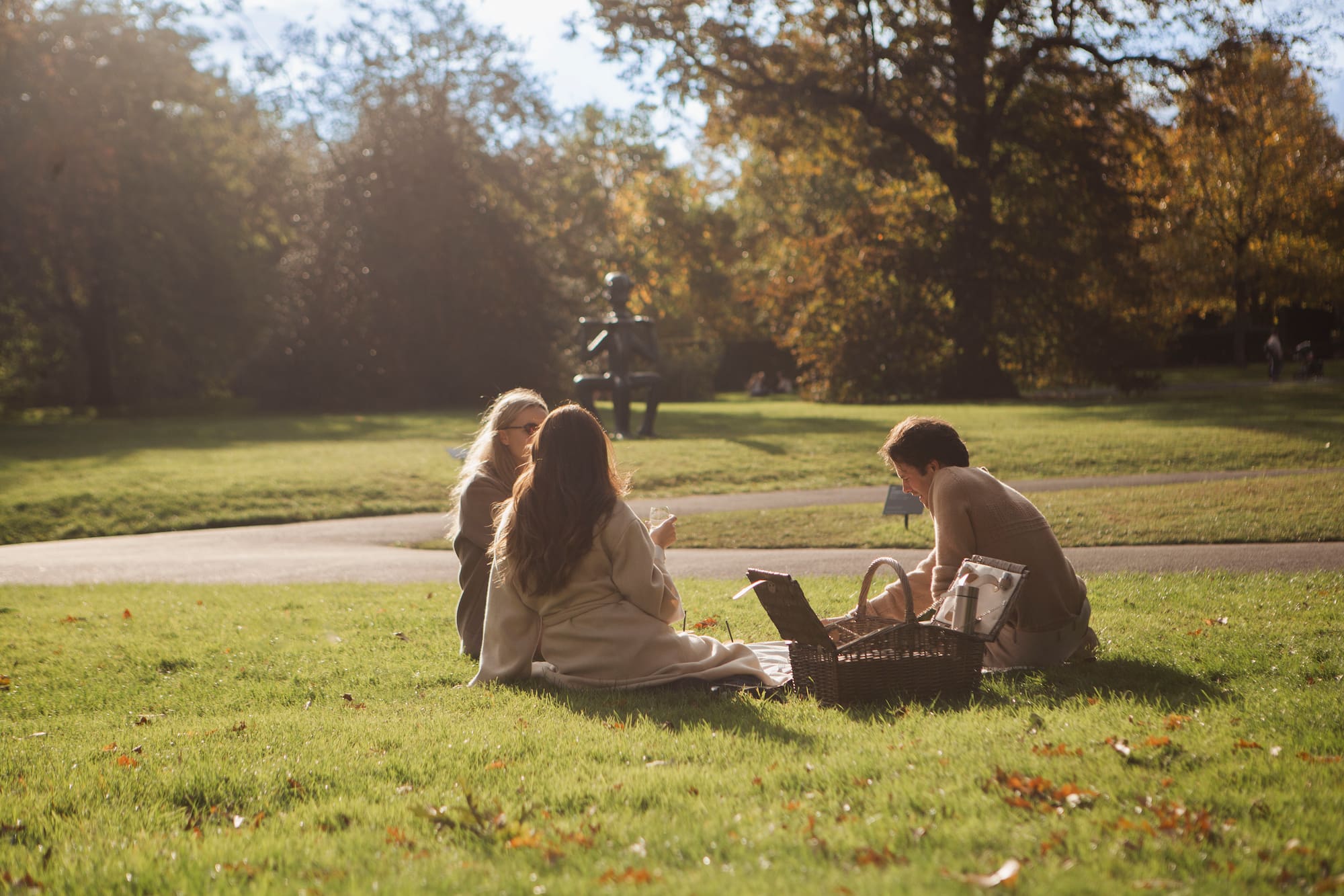 Three women enjoying a park picnic on green grass in autumn sun.