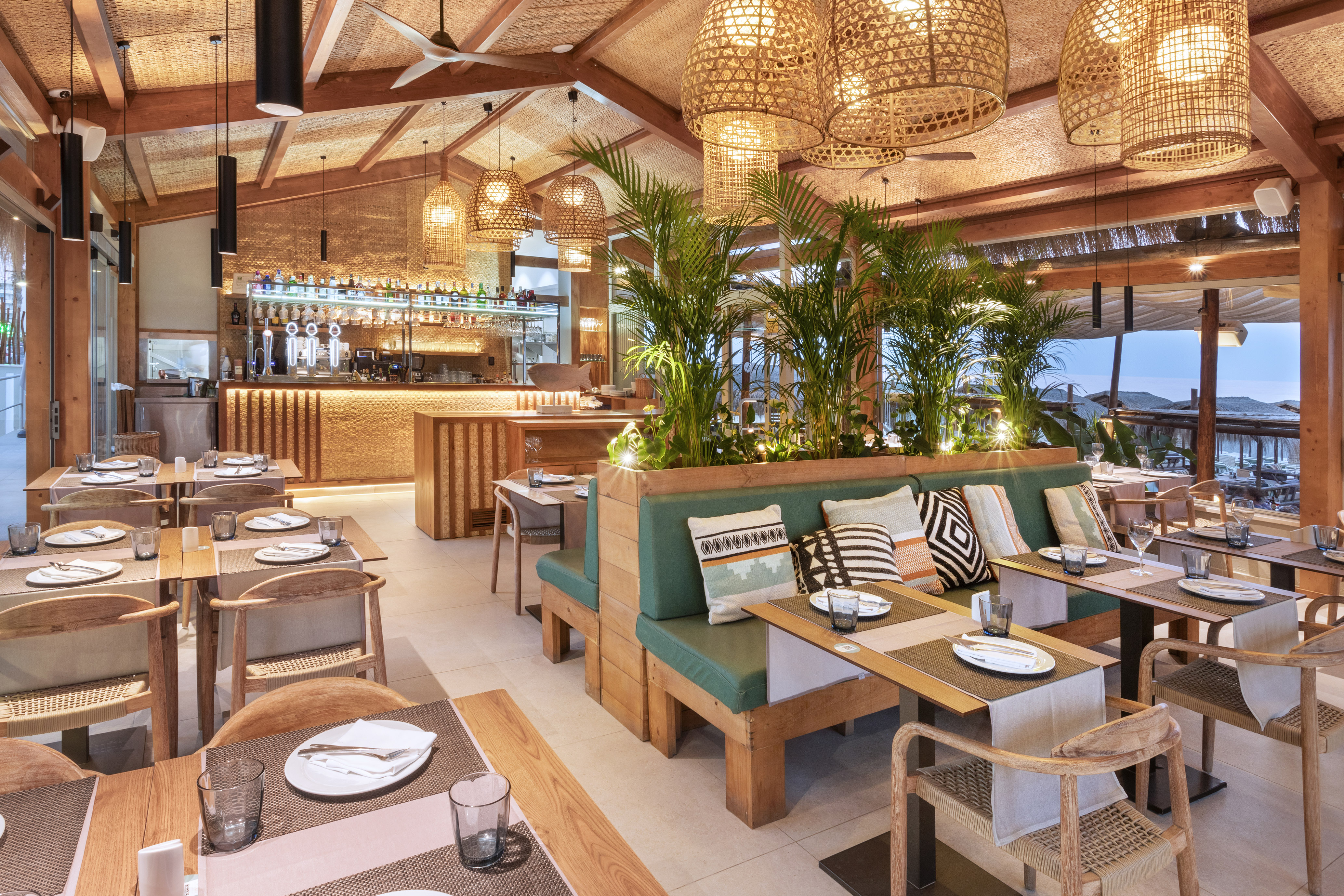 Tropical dining room with green booths, wooden tables, rattan lights, bar.