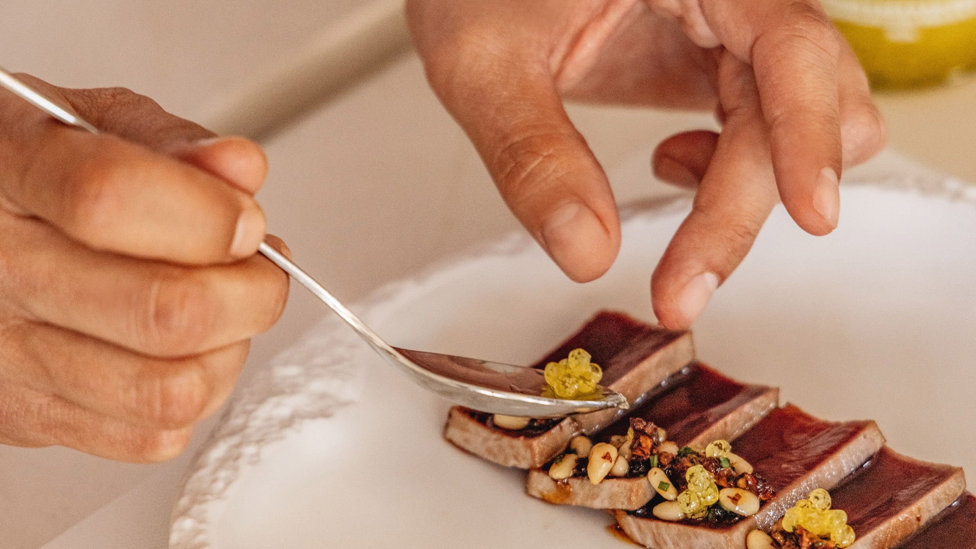 Chef emplatando tataki de atún gourmet con caviar cítrico y piñones.