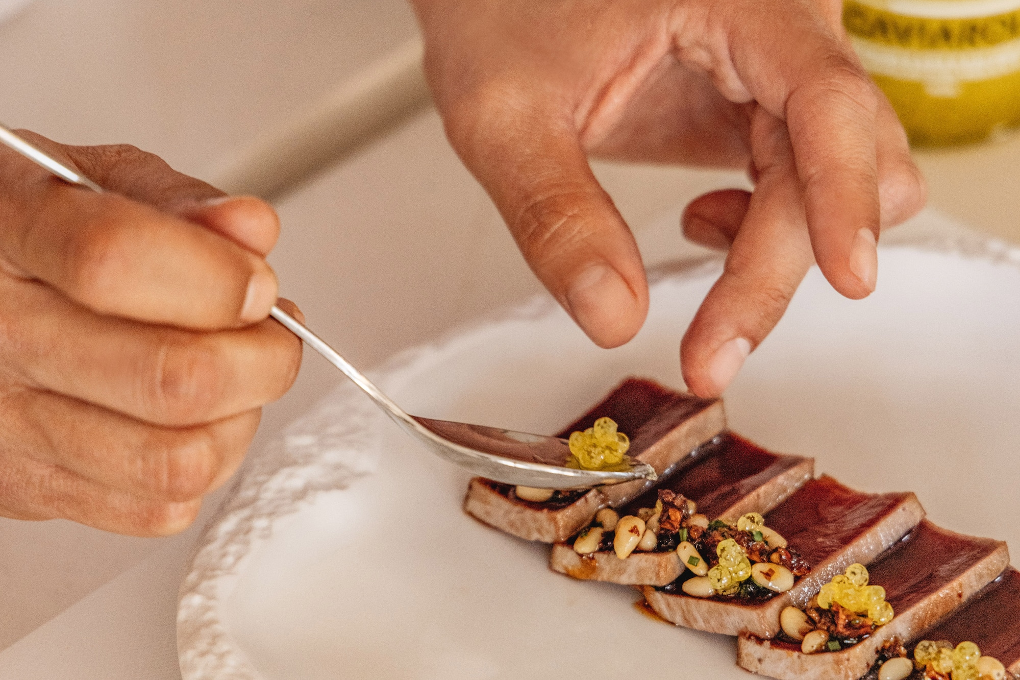 Chef emplatando tataki de atún gourmet con caviar cítrico y piñones.
