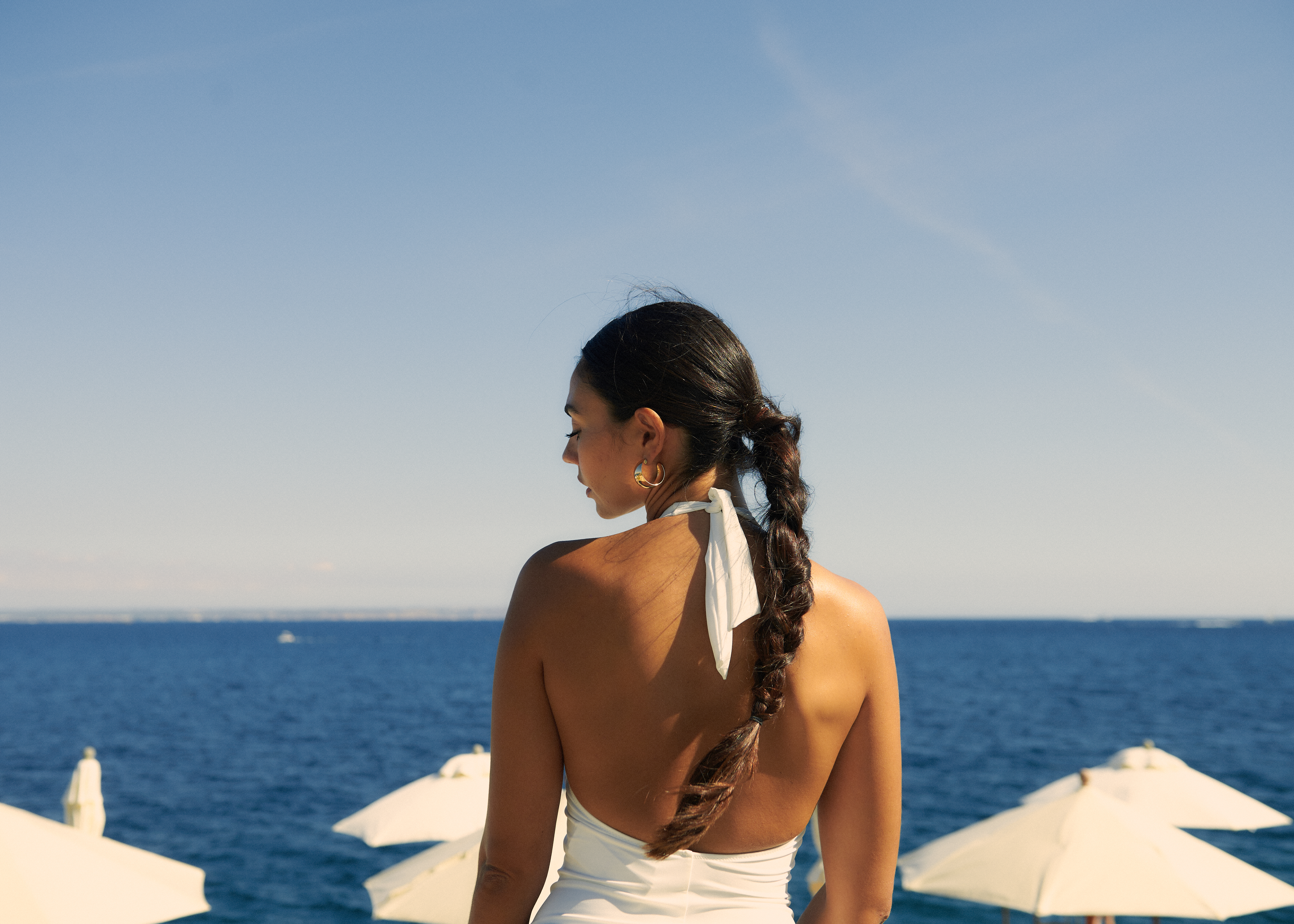 Woman in white halter top with braid by blue sea and sunny sky.