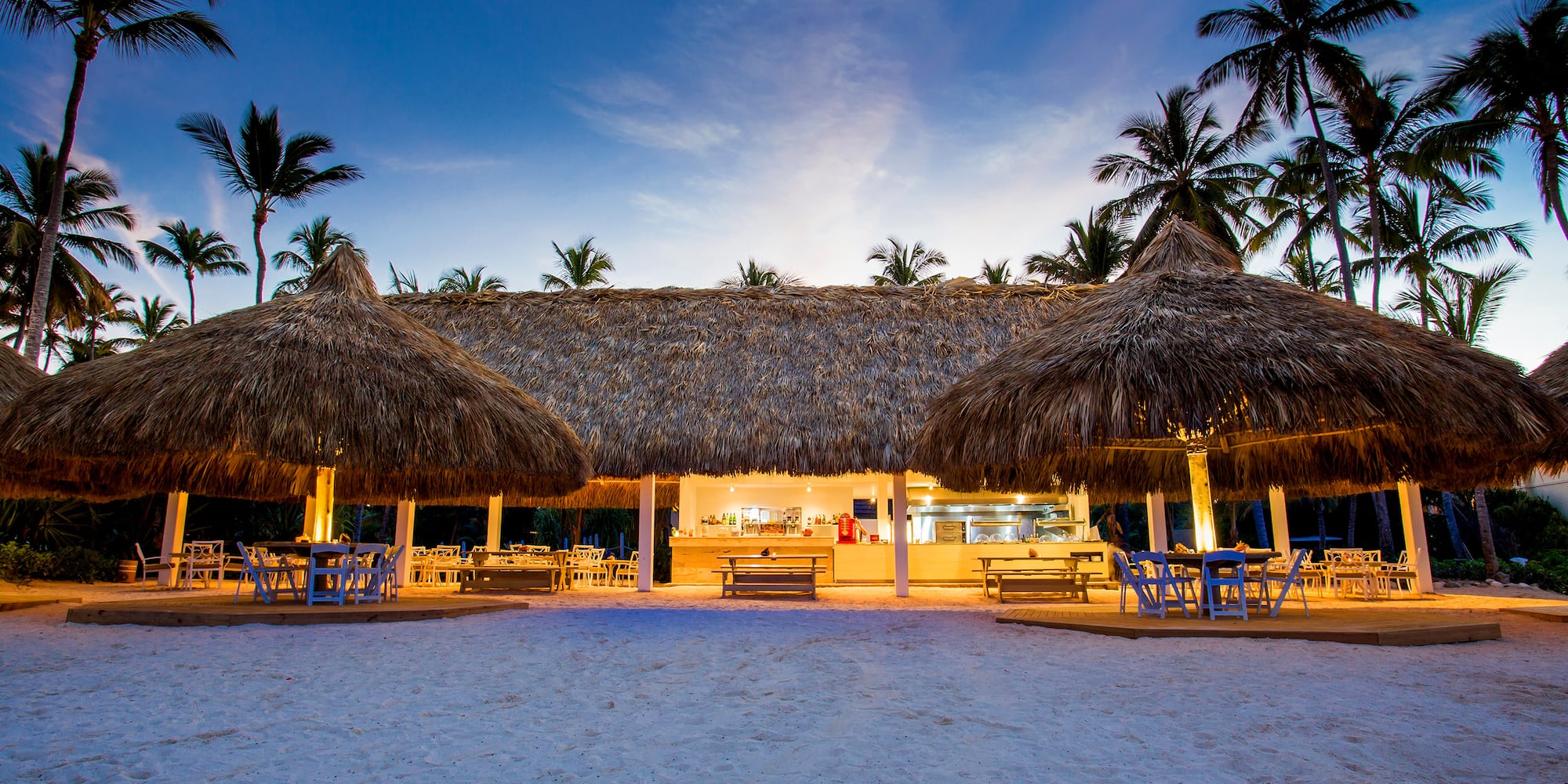 a building with thatched roof and tables and chairs on a beach
