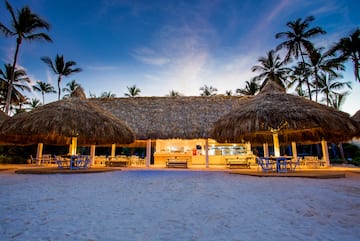 a building with thatched roof and tables and chairs on a beach