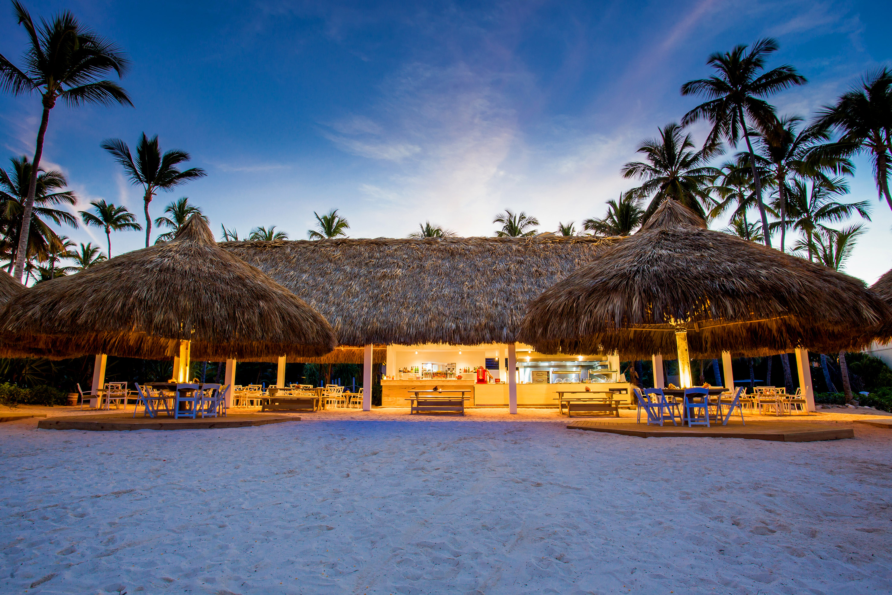 a building with thatched roof and tables and chairs on a beach