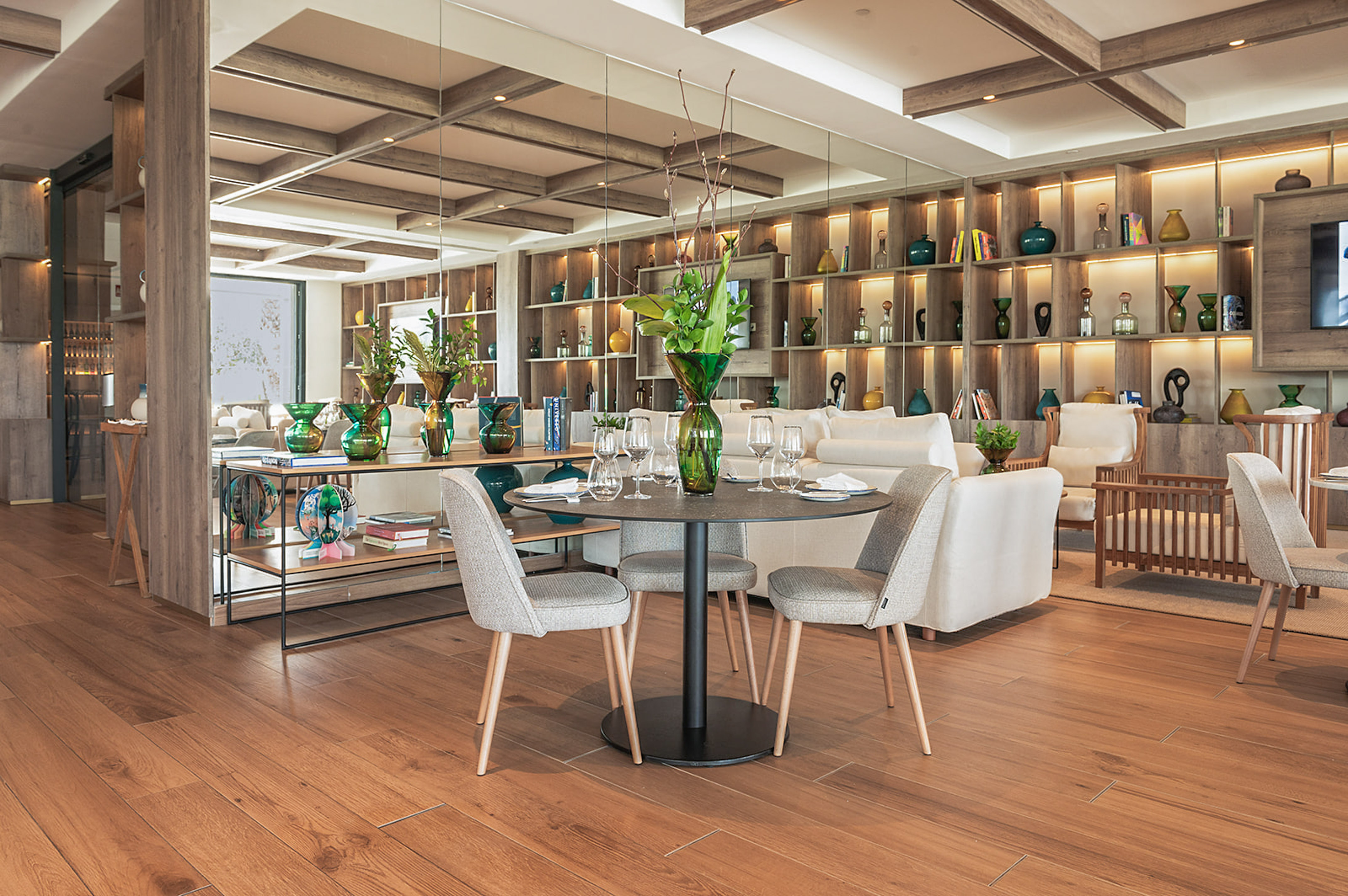 Chic dining and lounge area with wood floors, backlit shelves, and green vases.