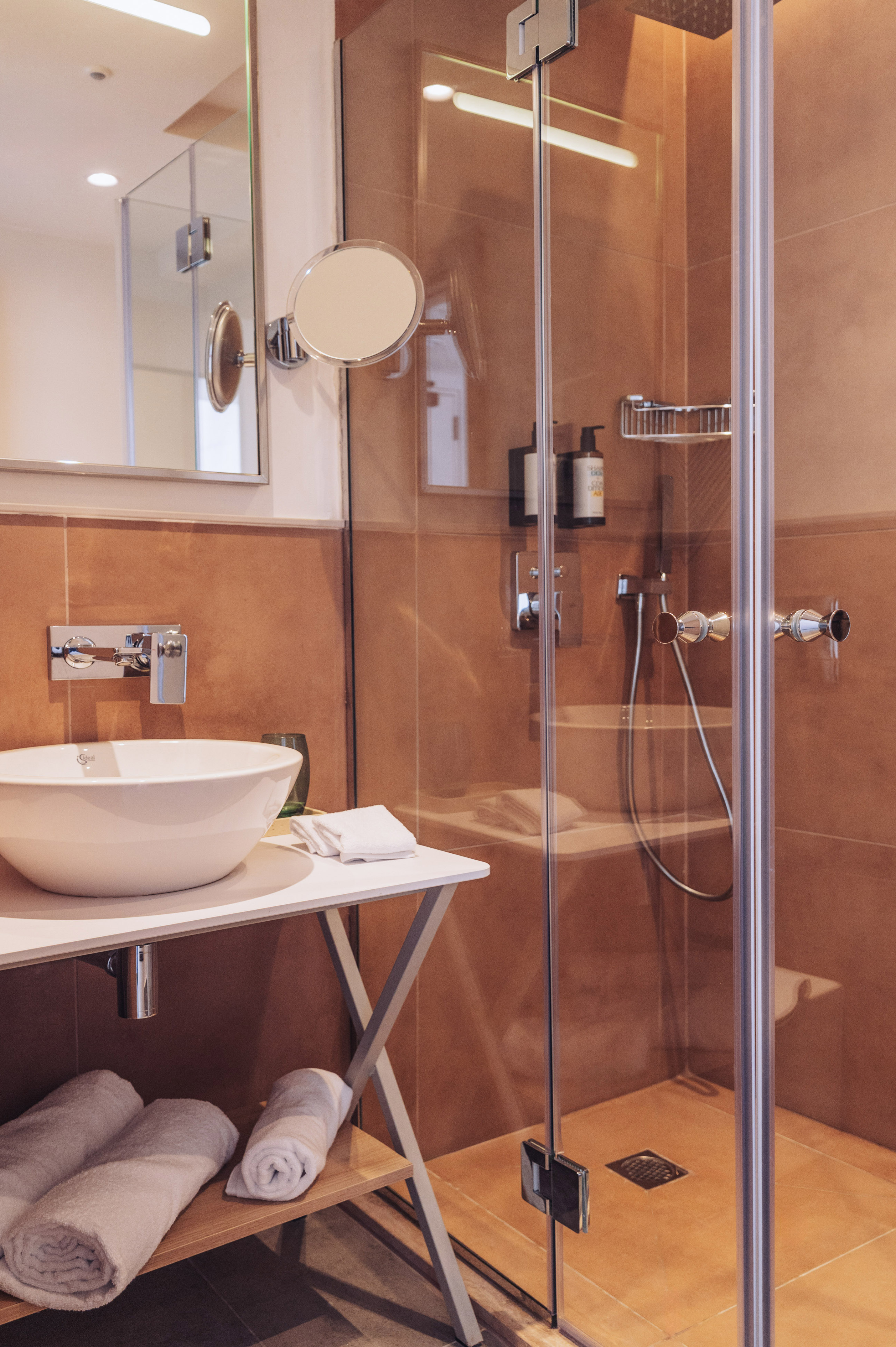 Modern bathroom with vessel sink, glass shower, brown tiles, and fresh towels.