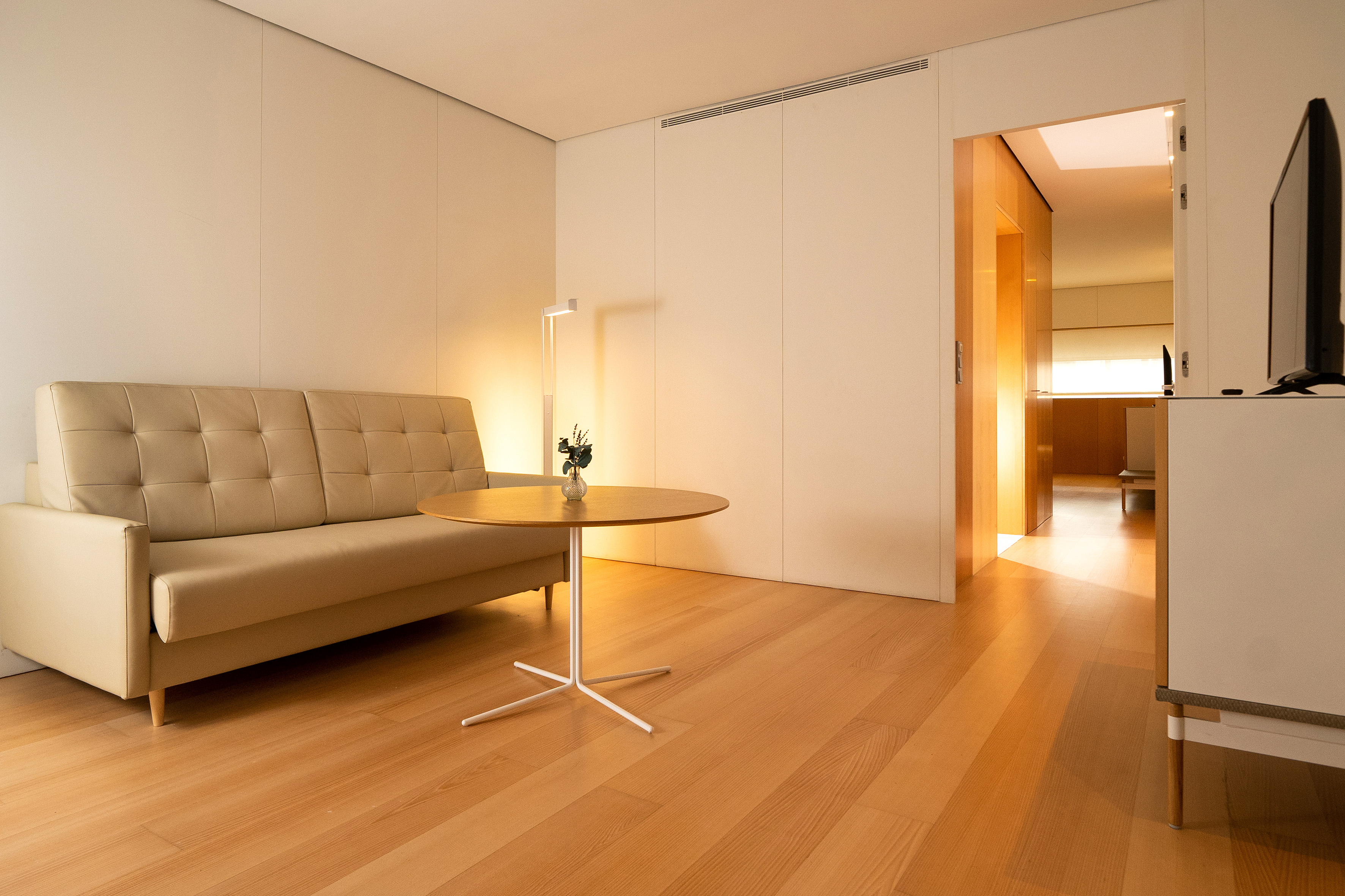 Modern hotel living room with beige sofa, wood floor, and minimalist decor.