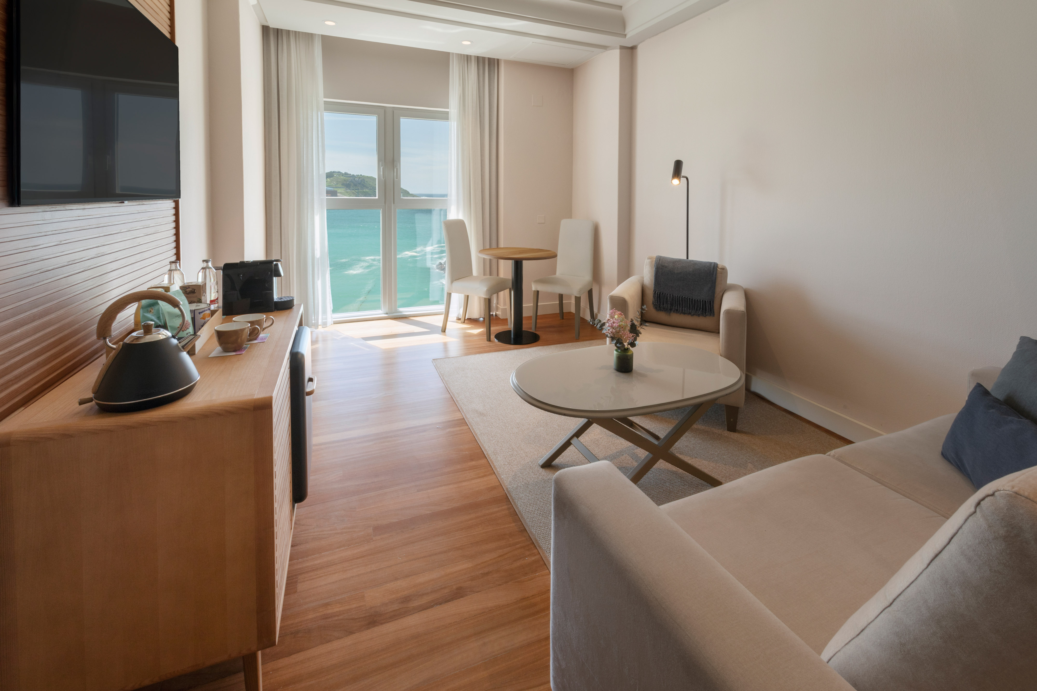 Salón de suite moderno con vistas al mar, sofá, mesa y cafetera.