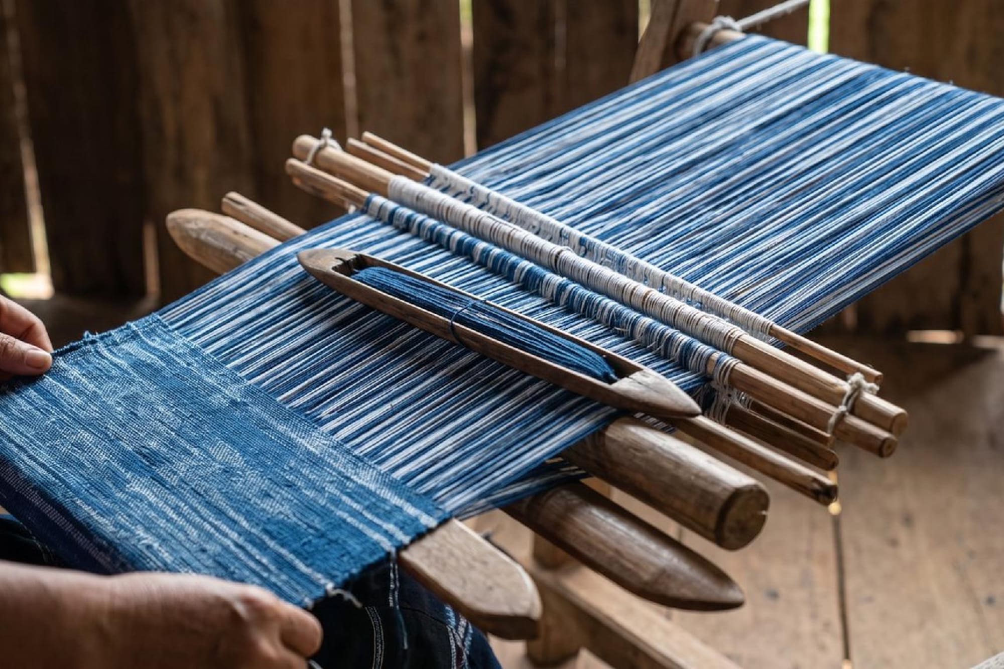 Hand weaving indigo blue and white striped fabric on a traditional loom.