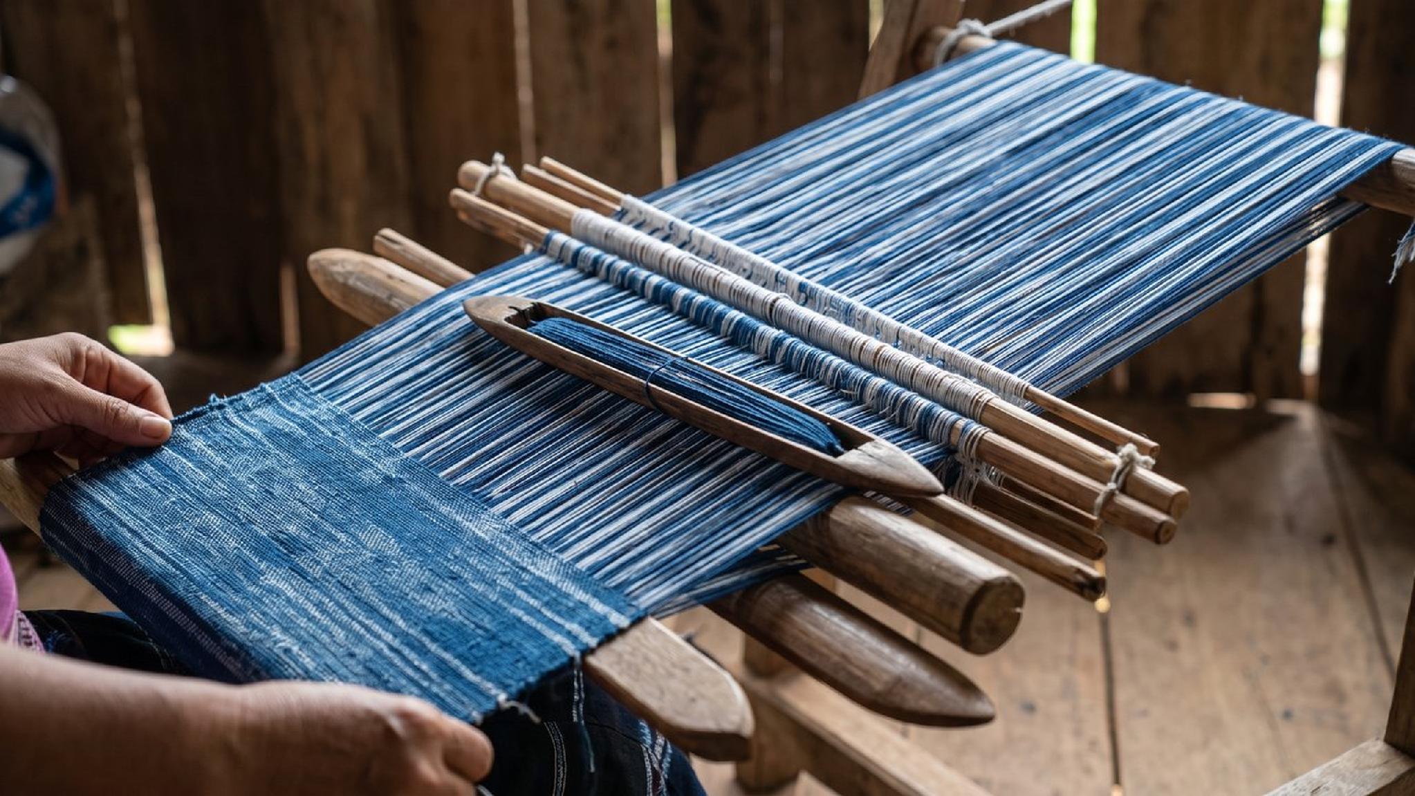 Hand weaving indigo blue and white striped fabric on a traditional loom.