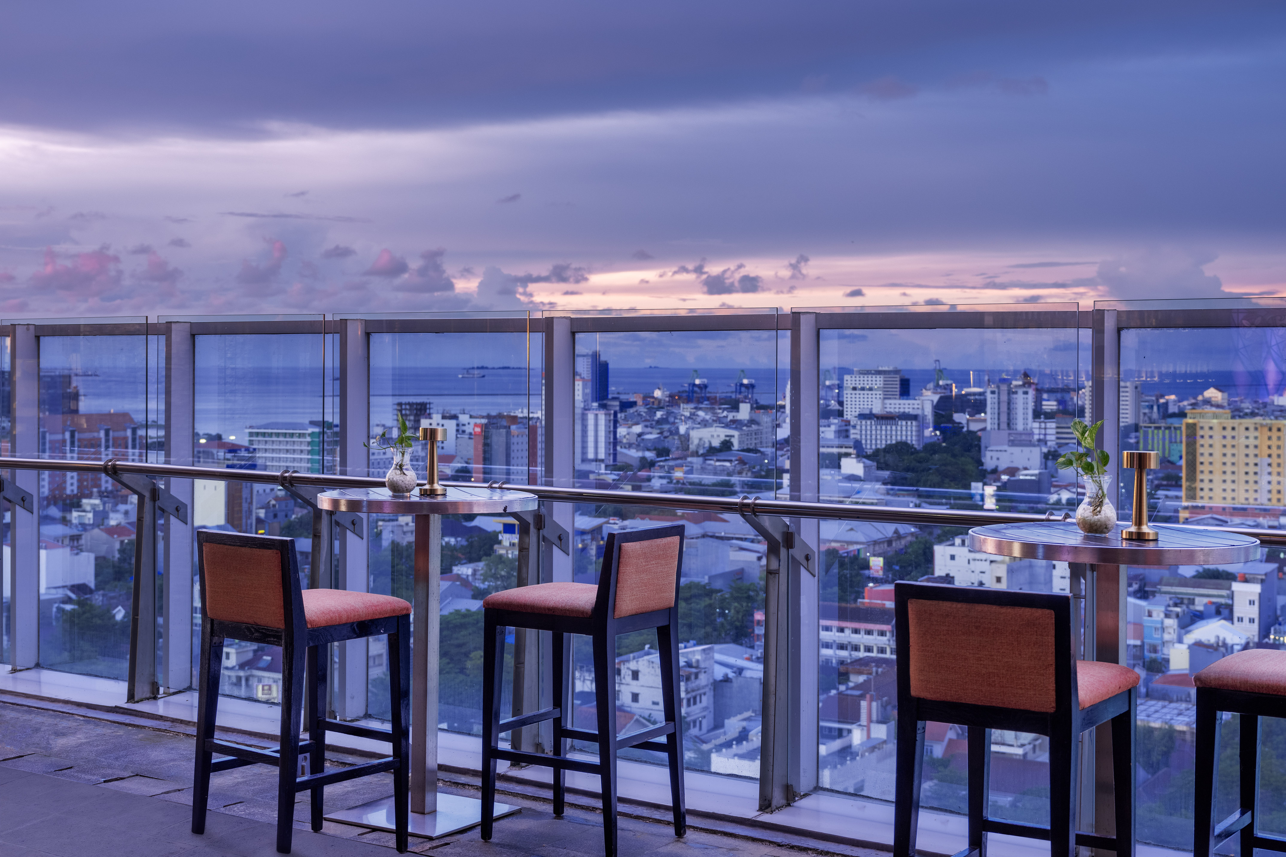 Evening rooftop bar overlooking city skyline and ocean.