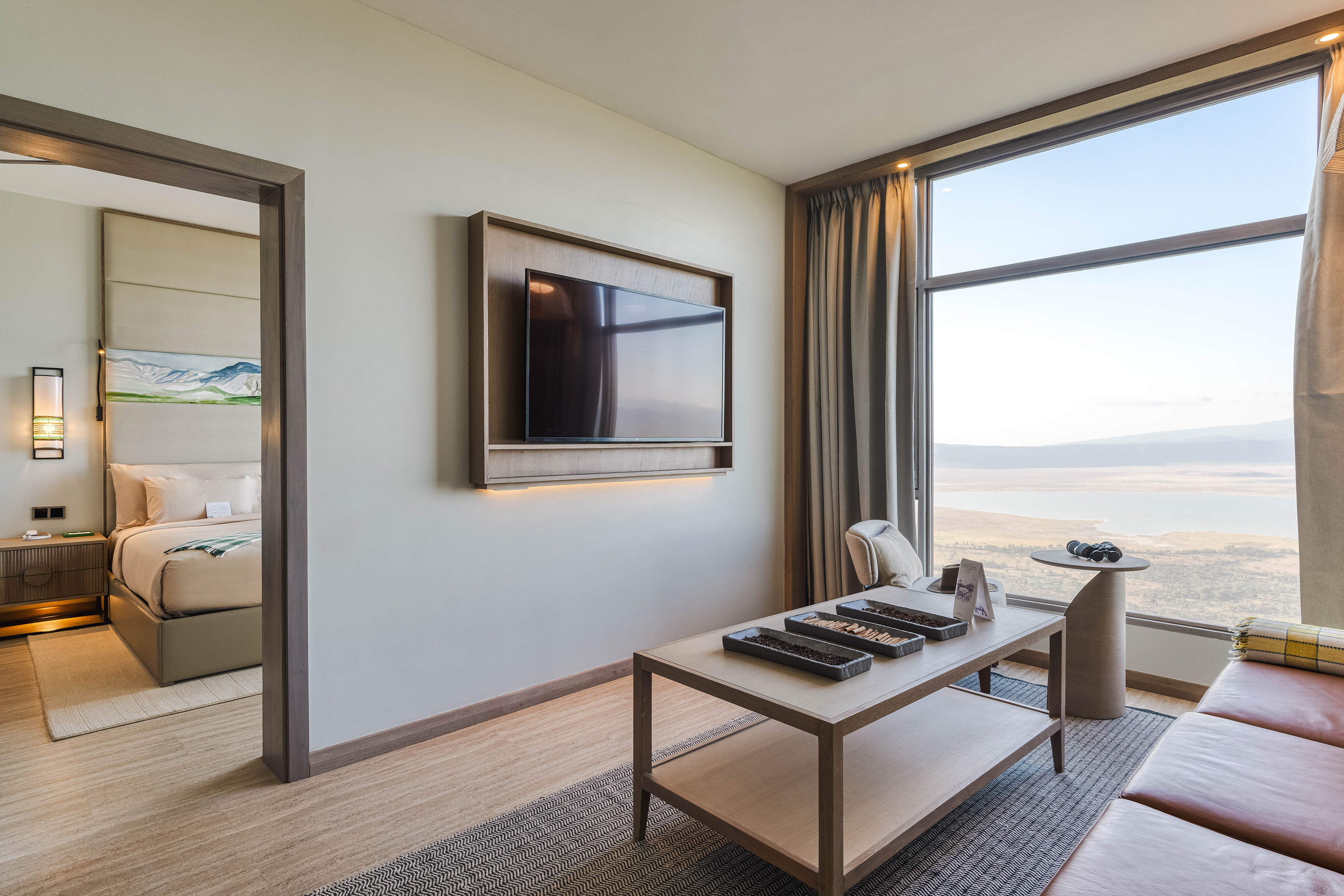 Modern hotel suite with lake view, bedroom, living area, and wall-mounted TV.