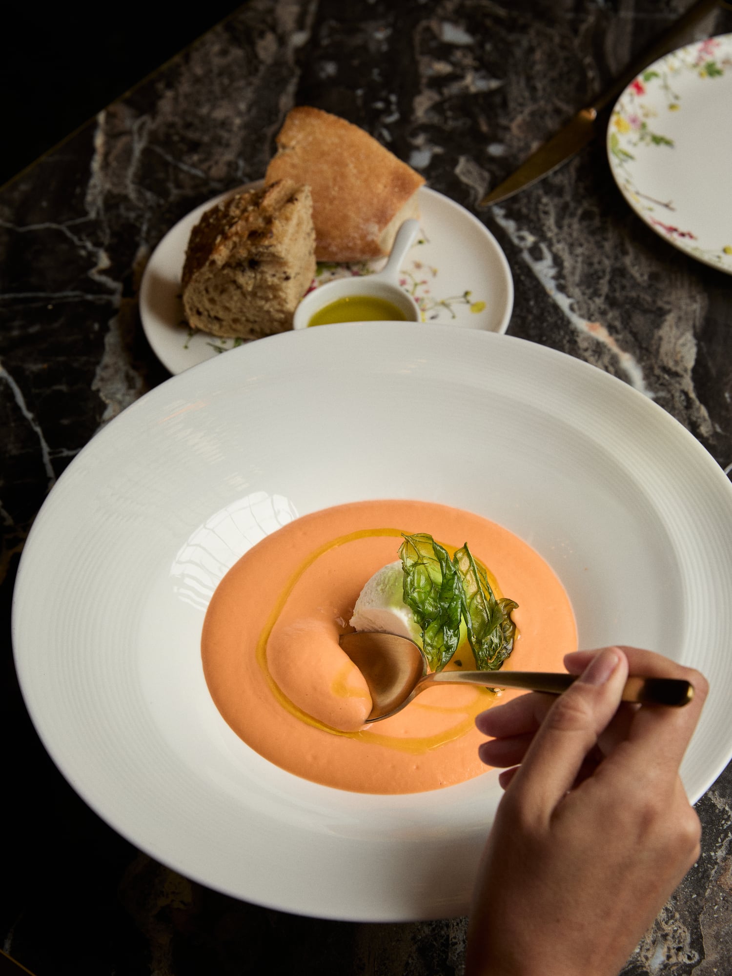 Eating peach soup with cream, basil, and olive oil; bread in background.