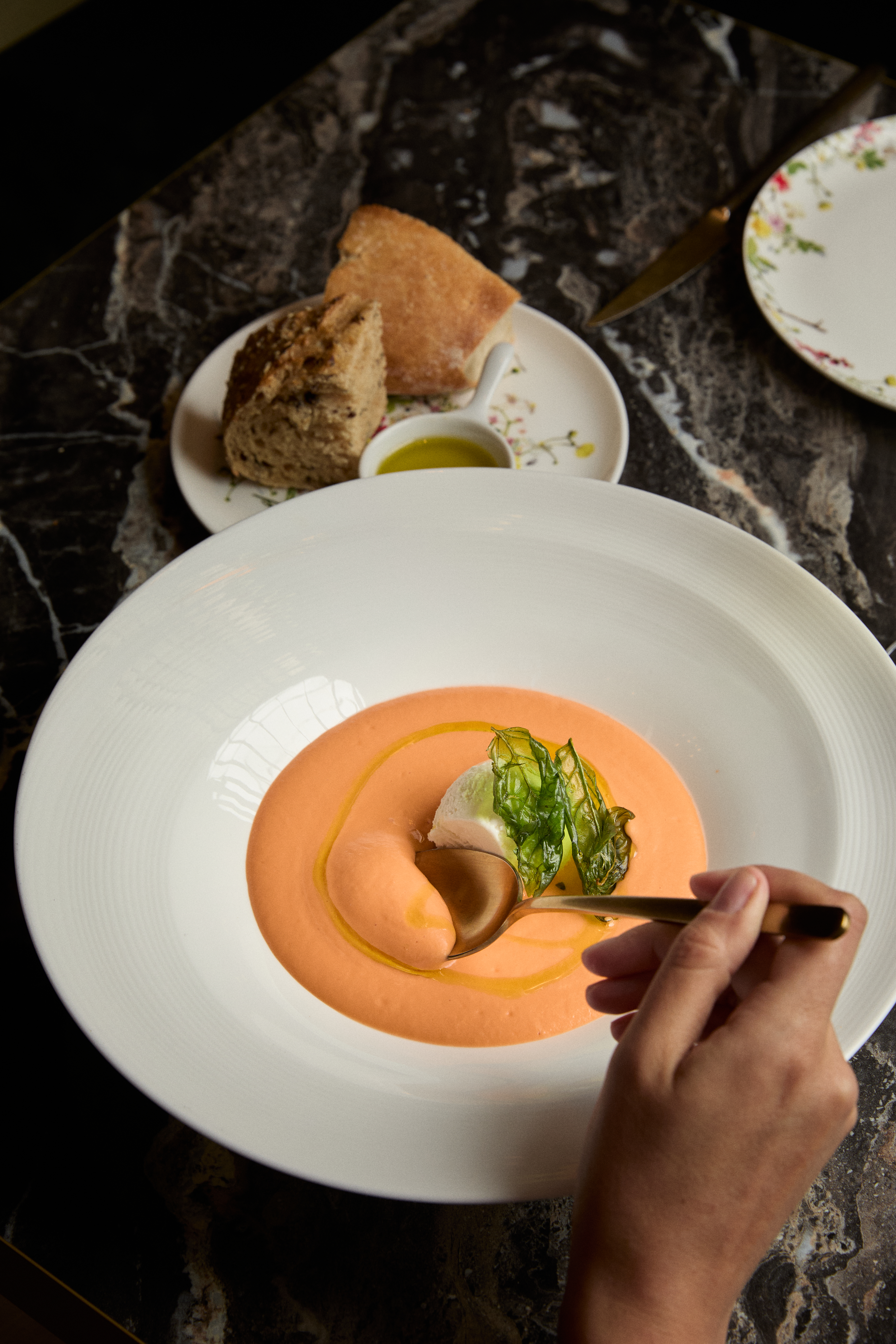 Eating peach soup with cream, basil, and olive oil; bread in background.