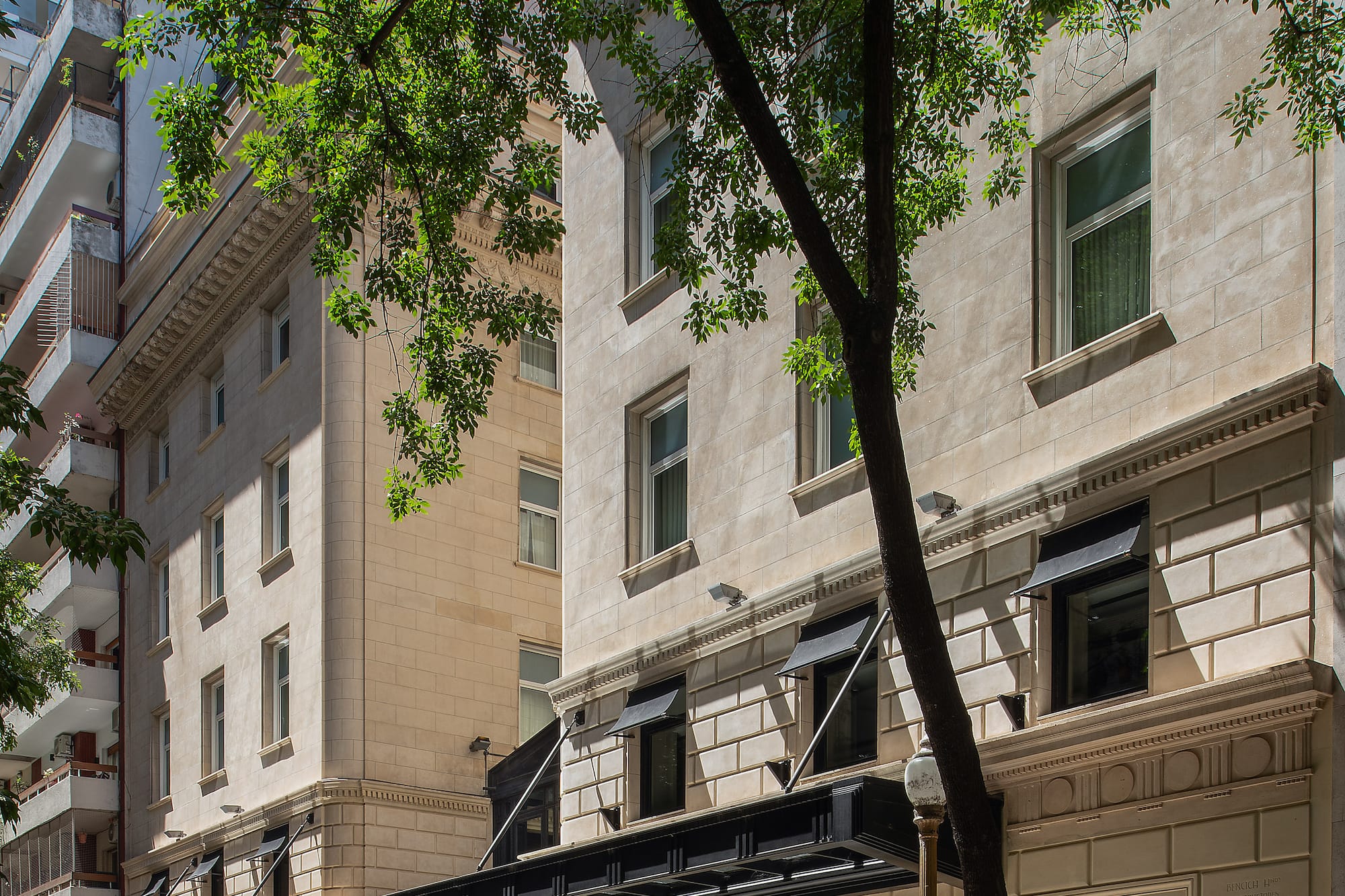 Casa Lucia hotel entrance, elegant stone facade, dark canopy, and street trees.