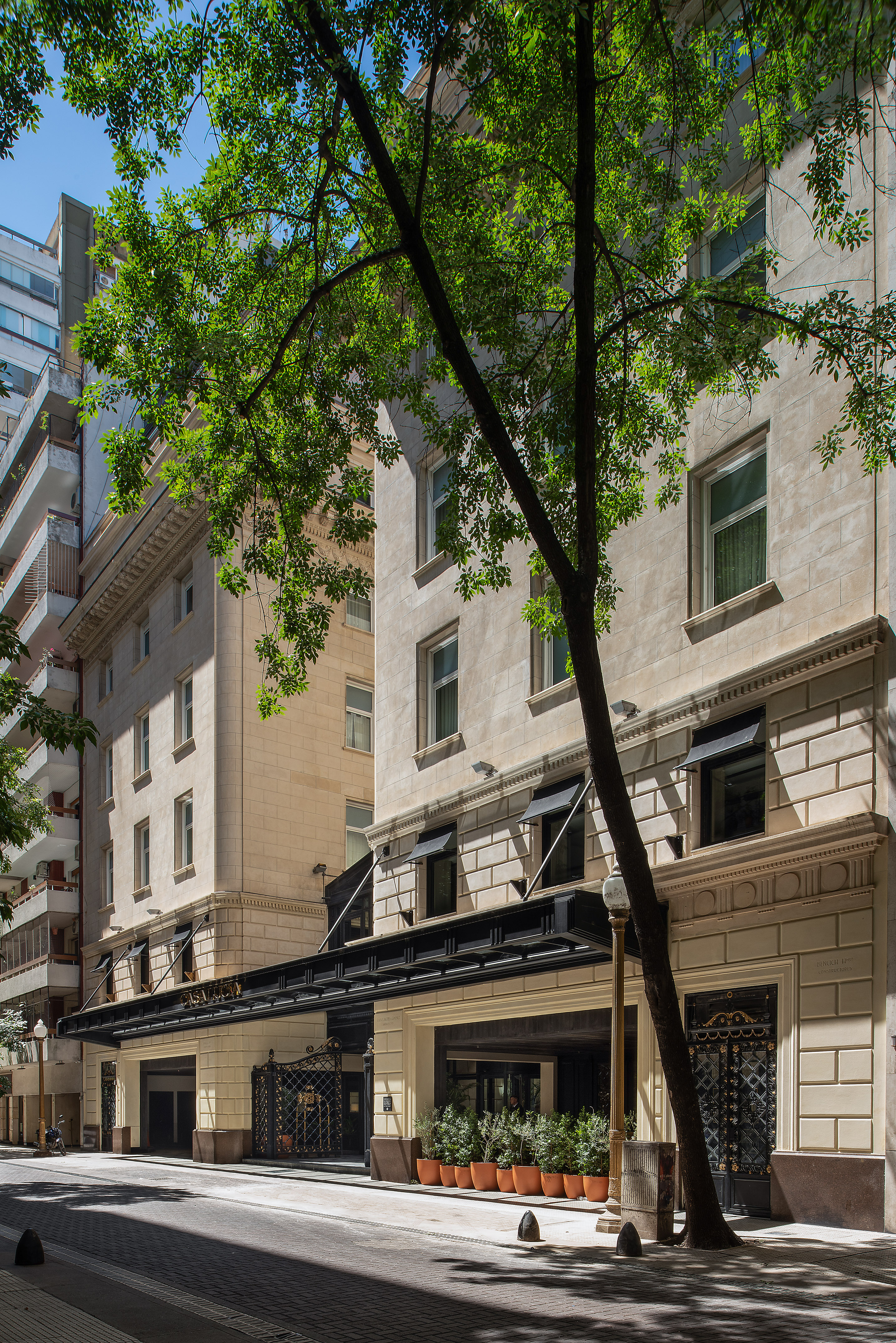 Casa Lucia hotel entrance, elegant stone facade, dark canopy, and street trees.